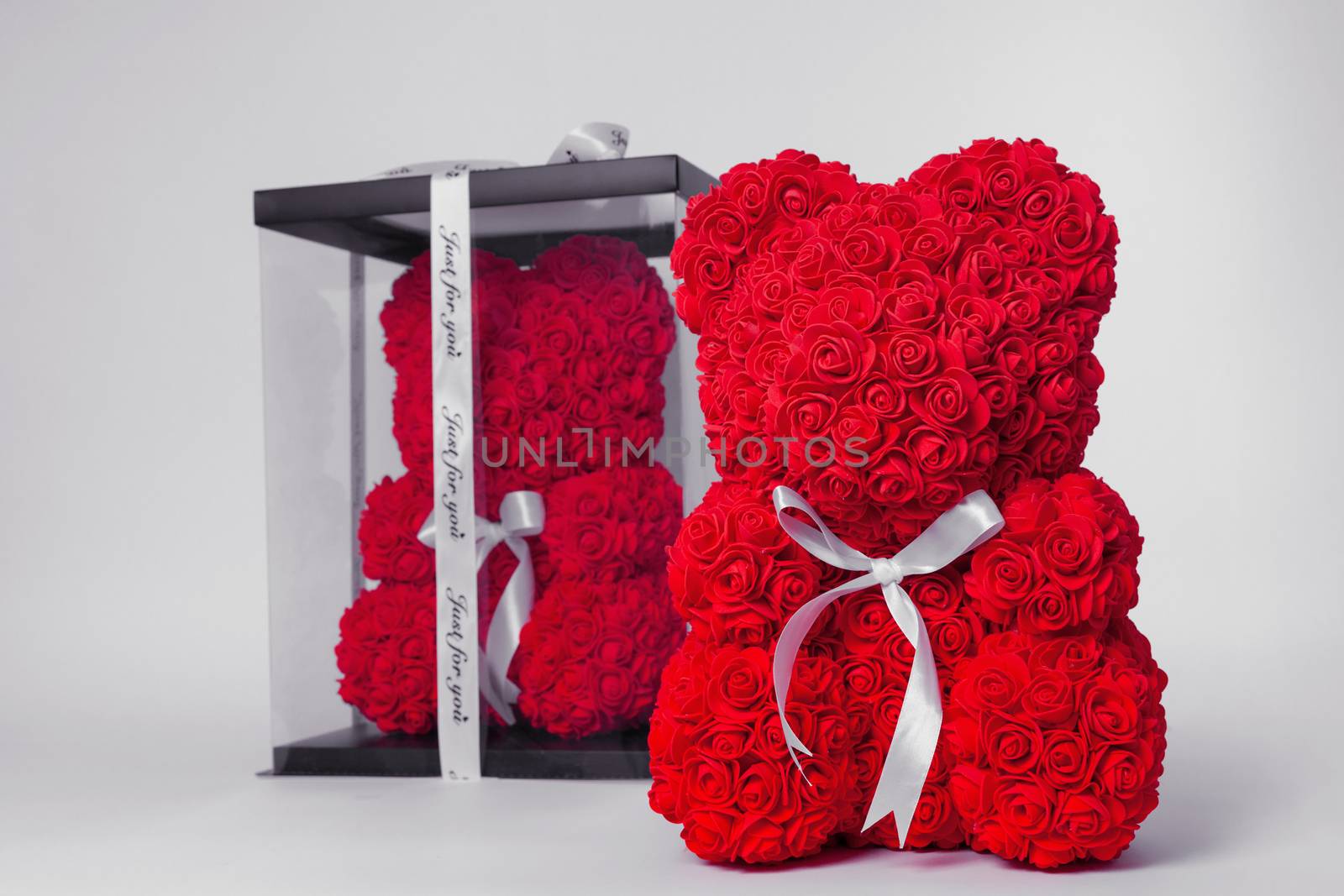 Red  teddy bear of foamirane roses. The same teddy in clear box with black paper cover on background. White stripe on teddy neck. Stock photo isolated on white background. by alexsdriver