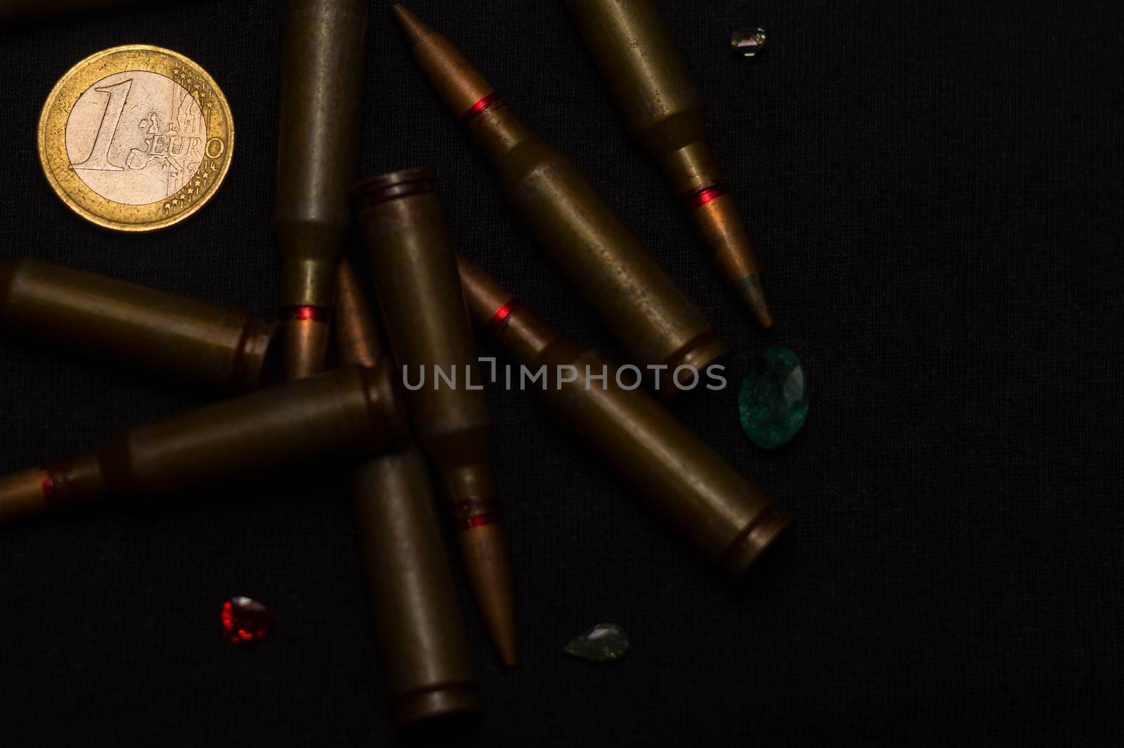 Rifle ammo around one euro coin wigh gemstones on black background. Symbolizes the war for money and one of the world's problems.