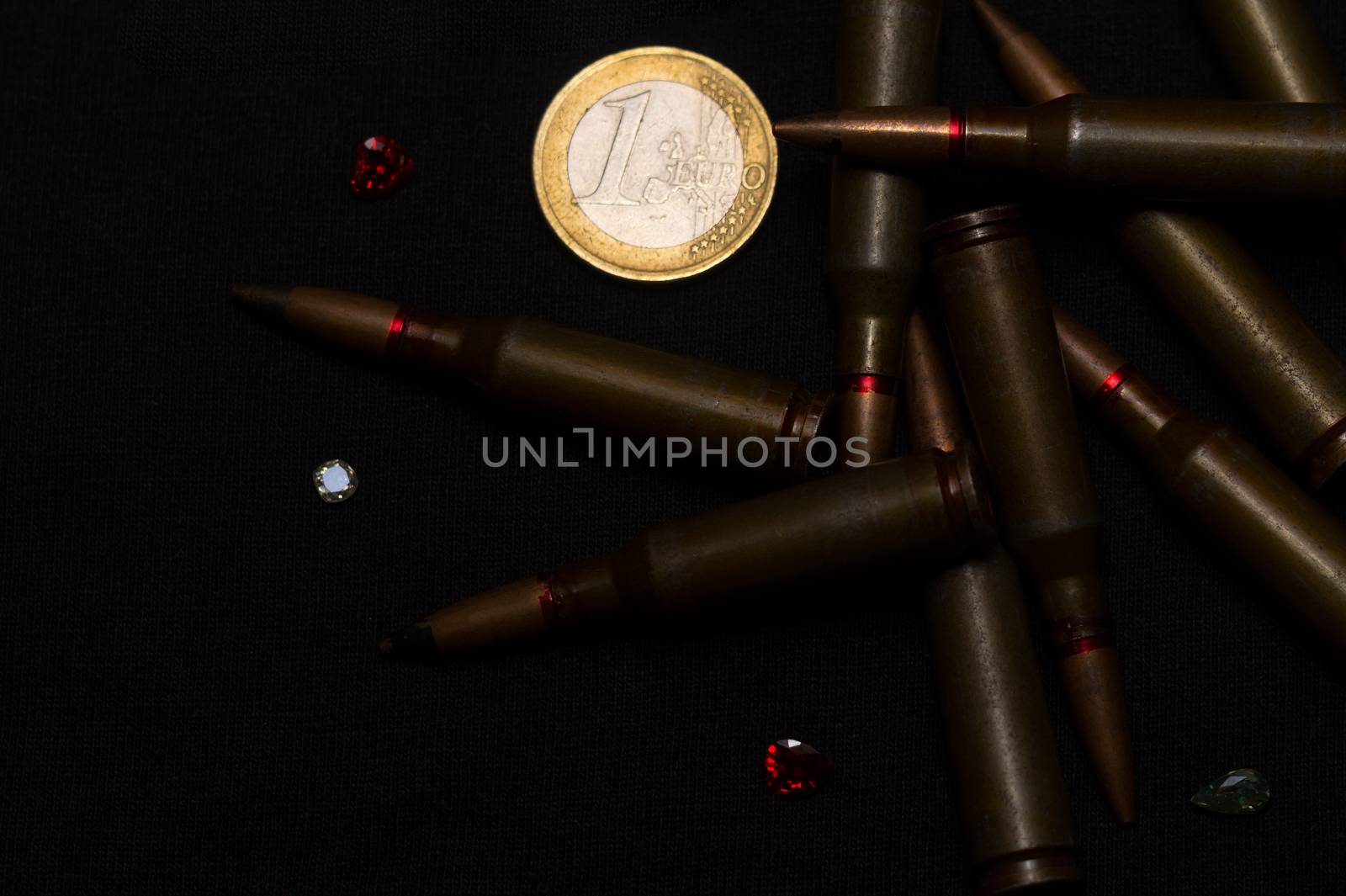 Rifle ammo around one euro coin wigh gemstones on black background. Symbolizes the war for money and one of the world's problems. by alexsdriver