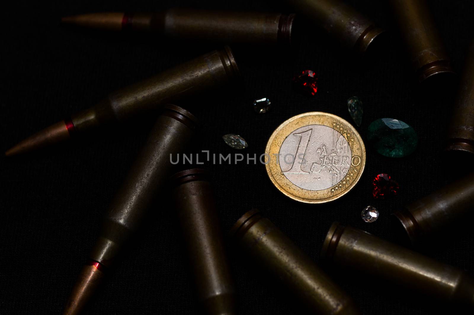 Rifle ammo with a lot of gemstones around one euro coin on black background. Symbolizes the war for money and one of the world's problems.