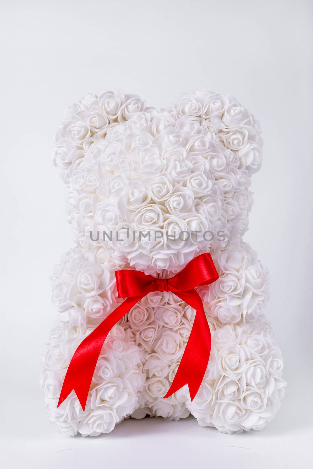 White teddy bear toy of foamirane roses. Red stripe on teddy neck. Stock photo isolated on white background. Gift on holiday for women.