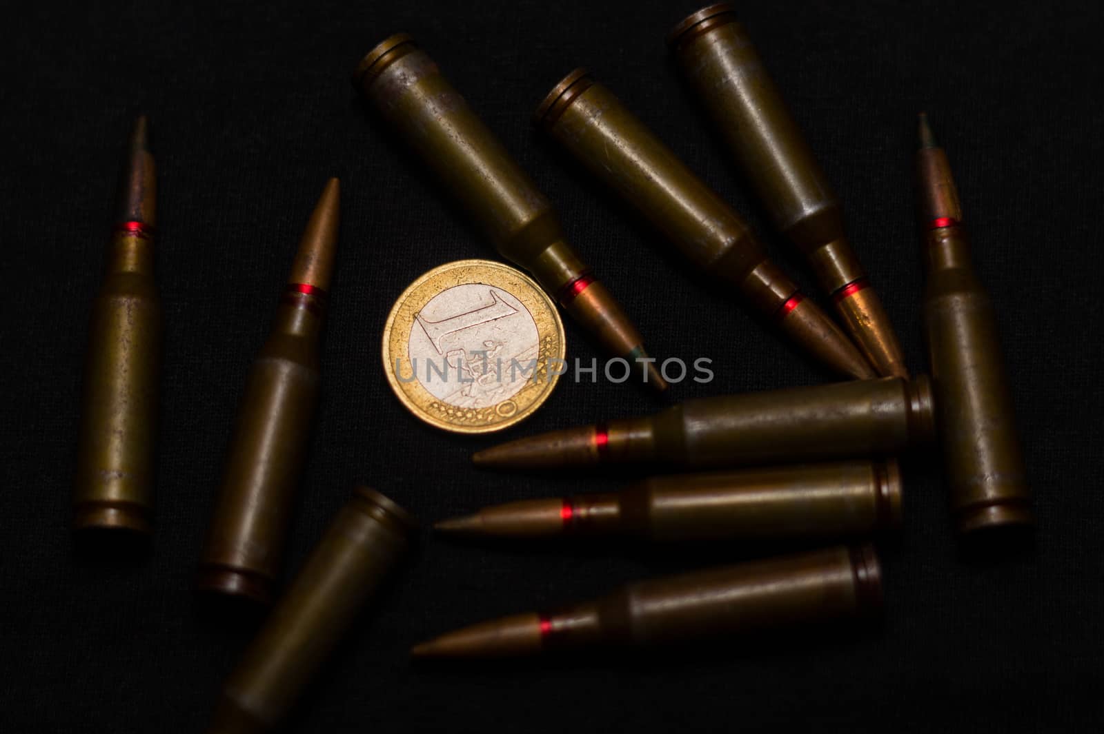 Rifle ammo around one euro coin on black background. Symbolizes the war for money and one of the world's problems.