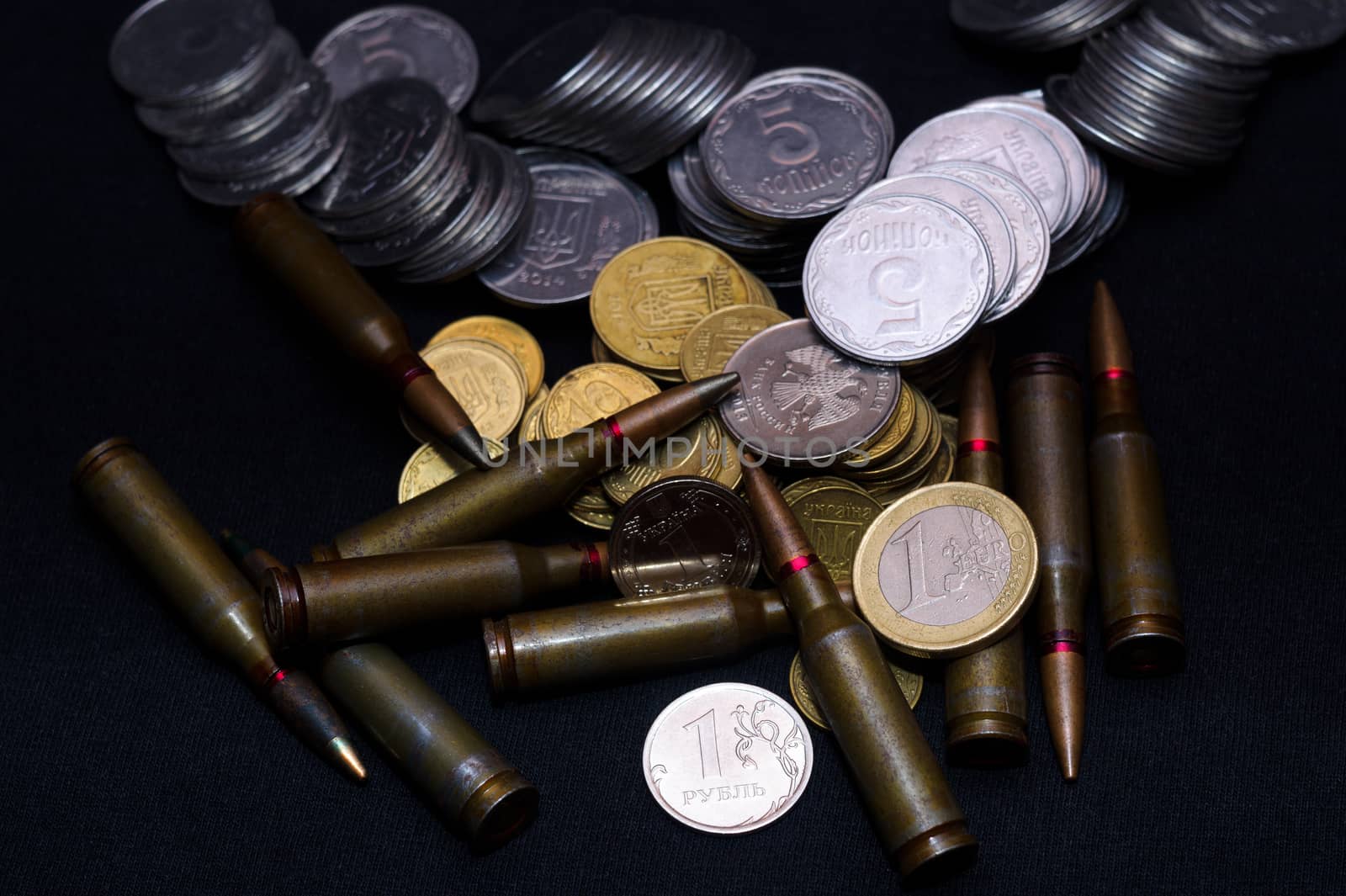One euro, Russian ruble and small Ukrainian coins with rifle military ammo on black background. Symbolizes war for money- biggest problem in world.