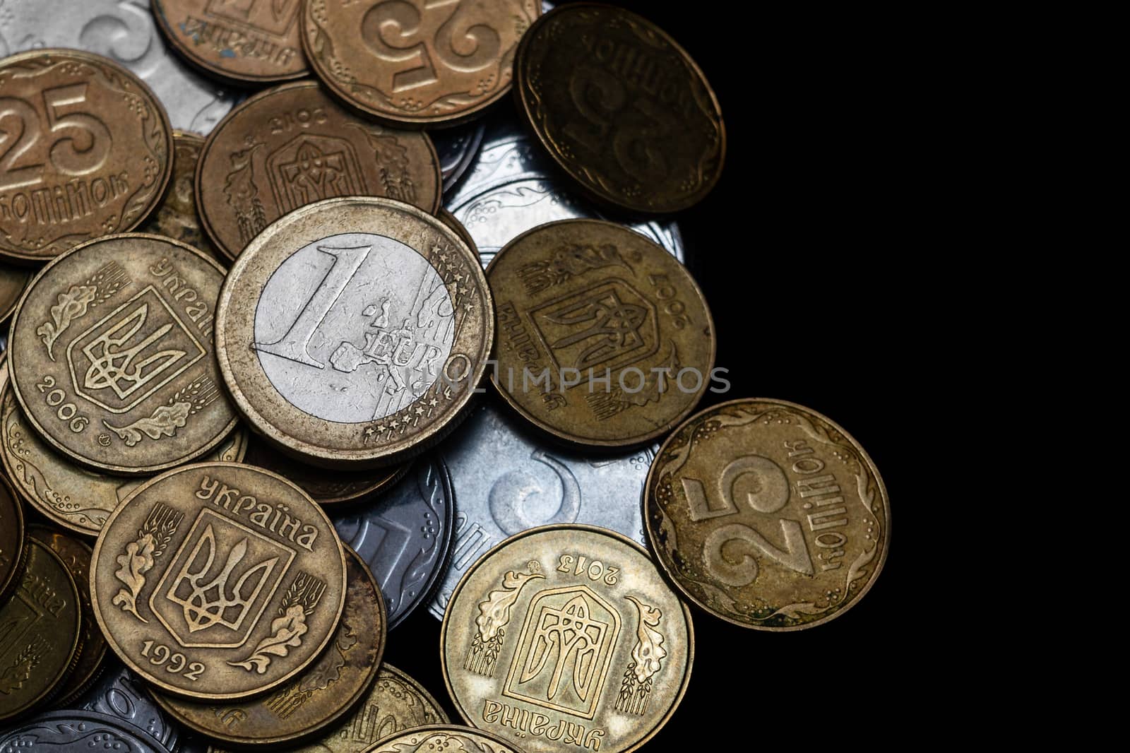 Ukrainian coins with one euro coin isolated on black background. Close-up view. Coins are located at the left side of frame. A conceptual image.