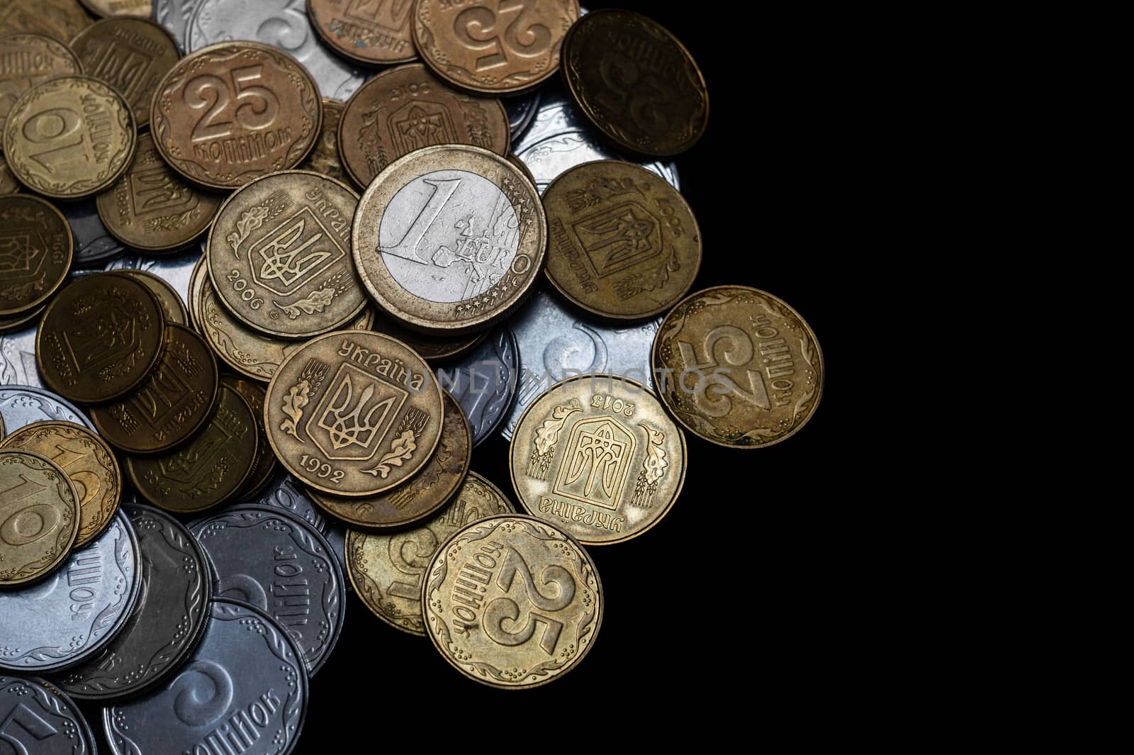 Ukrainian coins with one euro coin isolated on black background. Close-up view. Coins are located at the left side of frame. A conceptual image.