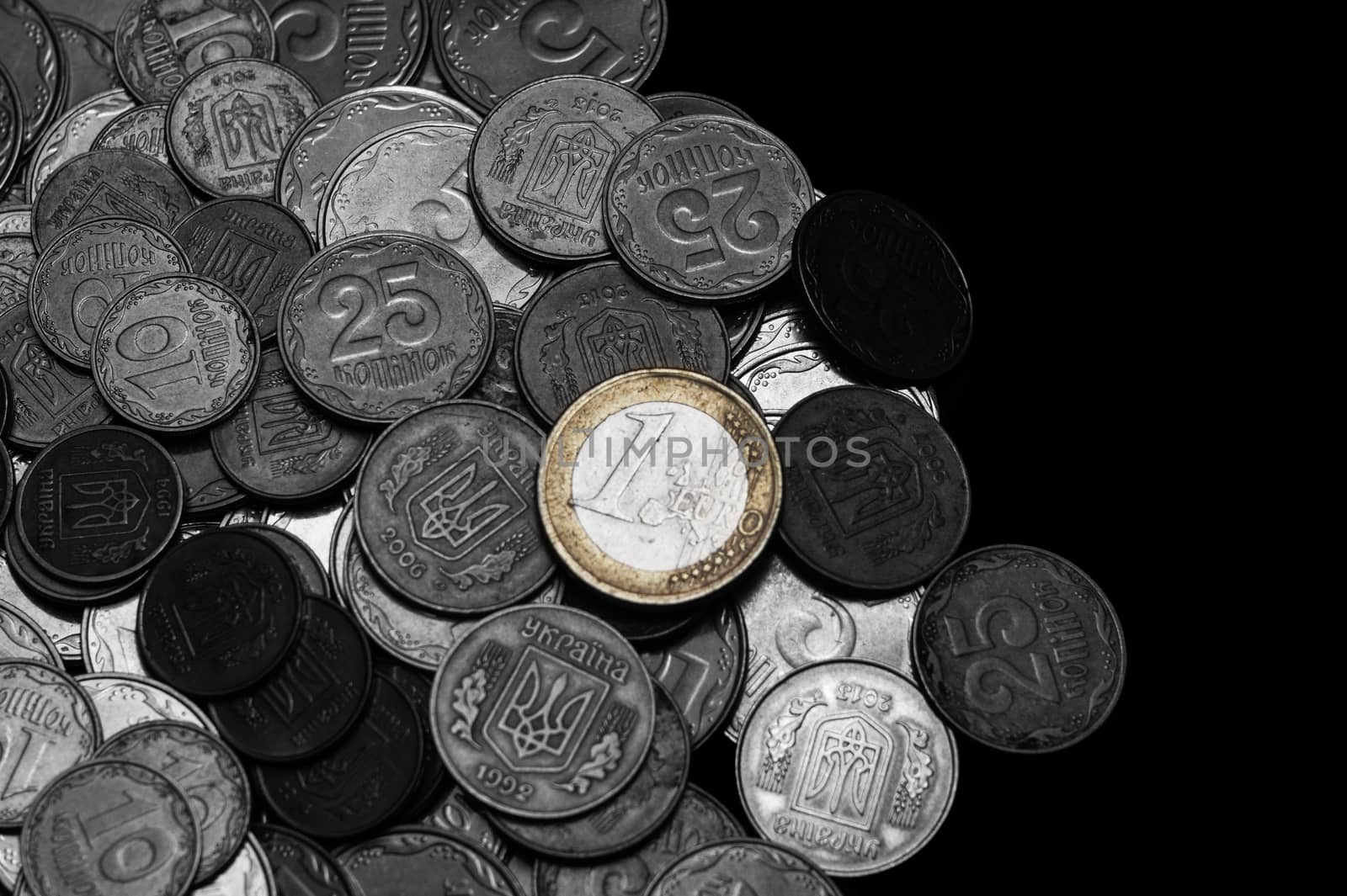 Ukrainian coins with one euro coin isolated on black background. Black and white image. Euro coin is colored. Close-up view. Coins are located at the left side of frame. A conceptual image.