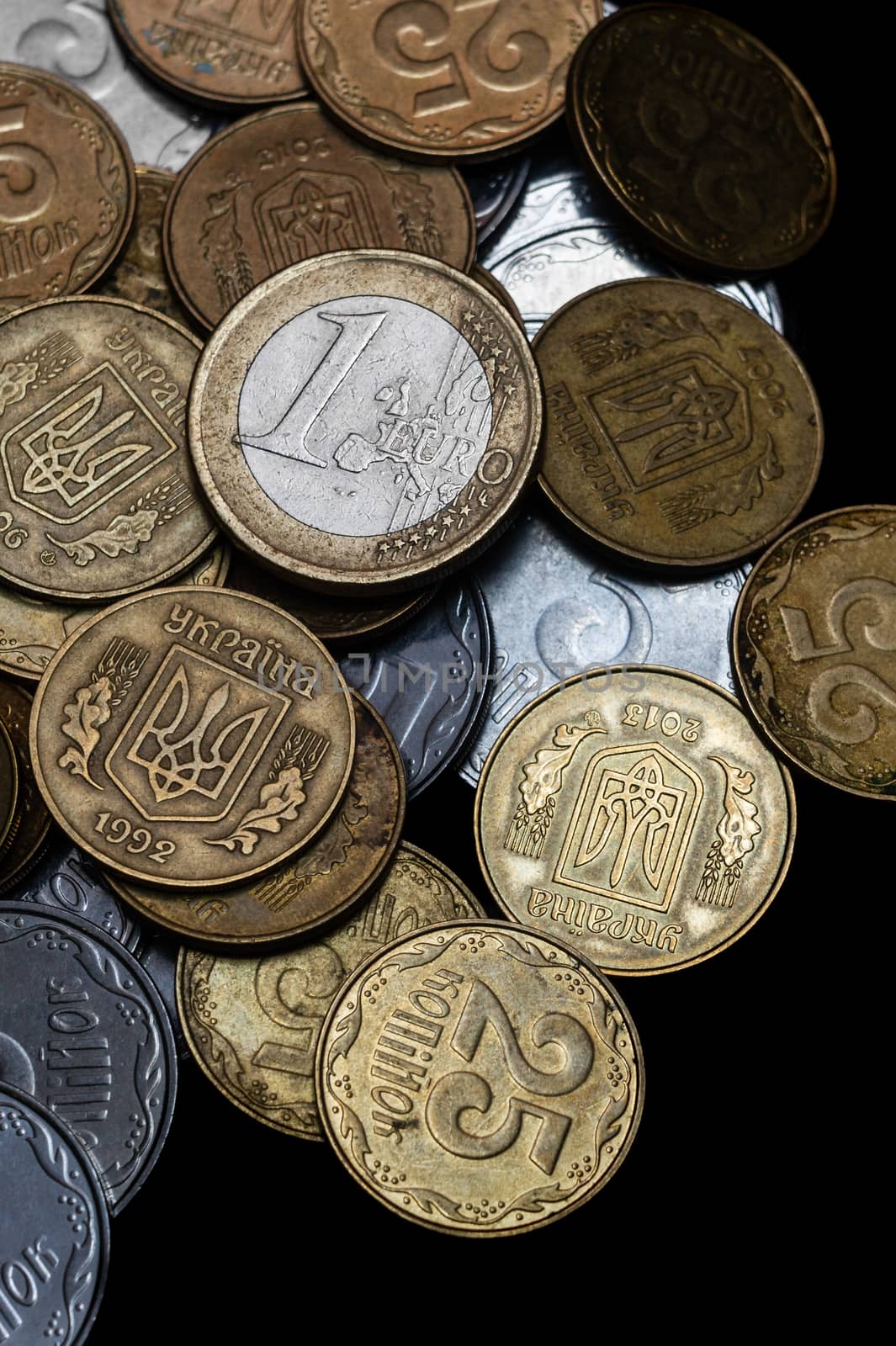 Ukrainian coins with one euro coin isolated on black background. Close-up view. Coins are located at center of frame. A conceptual image.