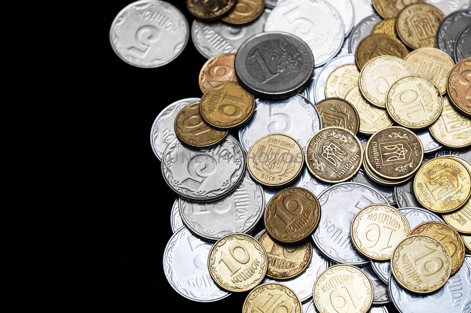 Ukrainian coins with one euro coin isolated on black background. Euro coin is uncolored. Close-up view. Coins are located at the right side of frame. A conceptual image.