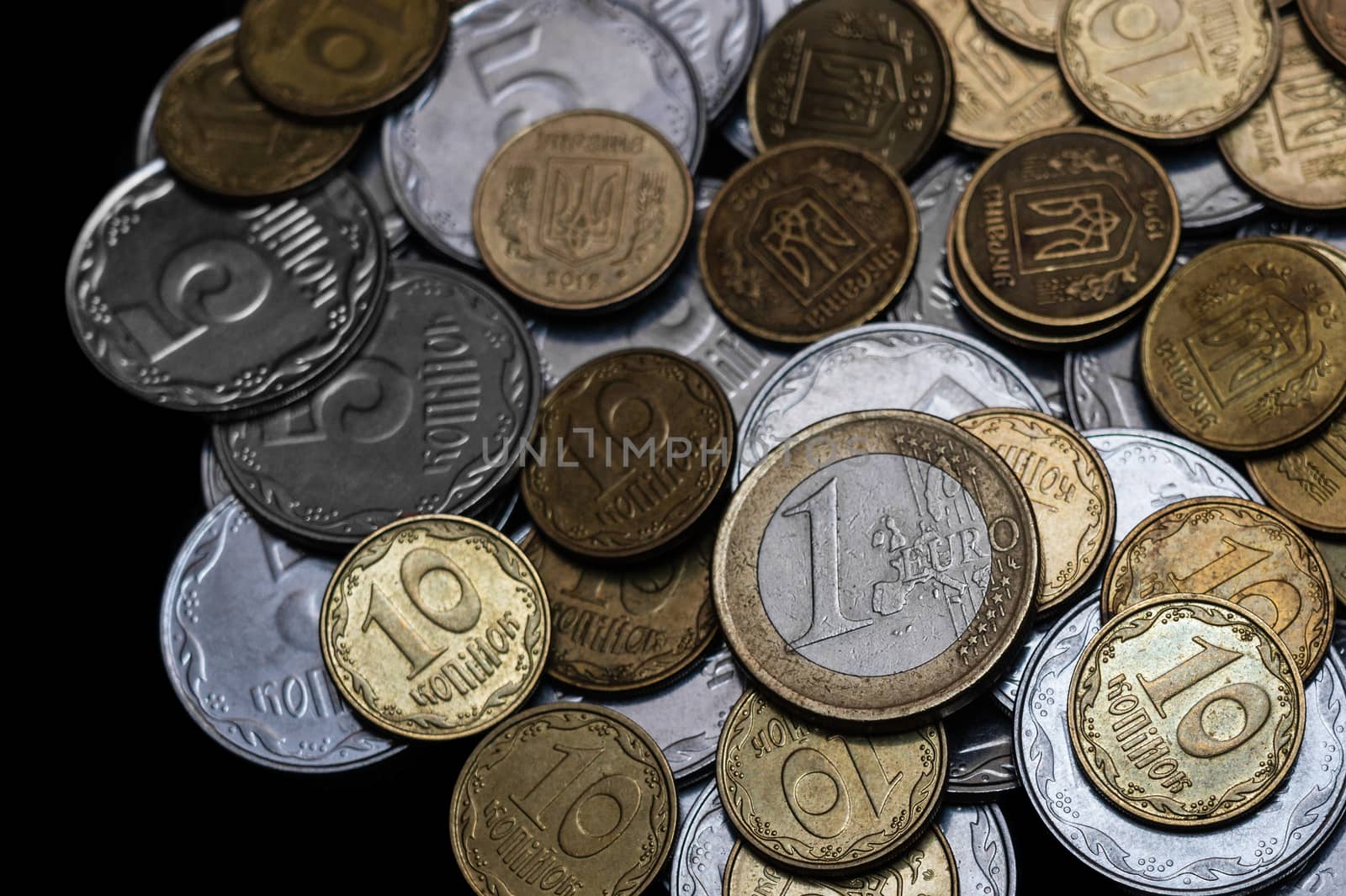 Ukrainian coins with one euro coin isolated on black background. Close-up view. Coins are located at center of frame. A conceptual image.