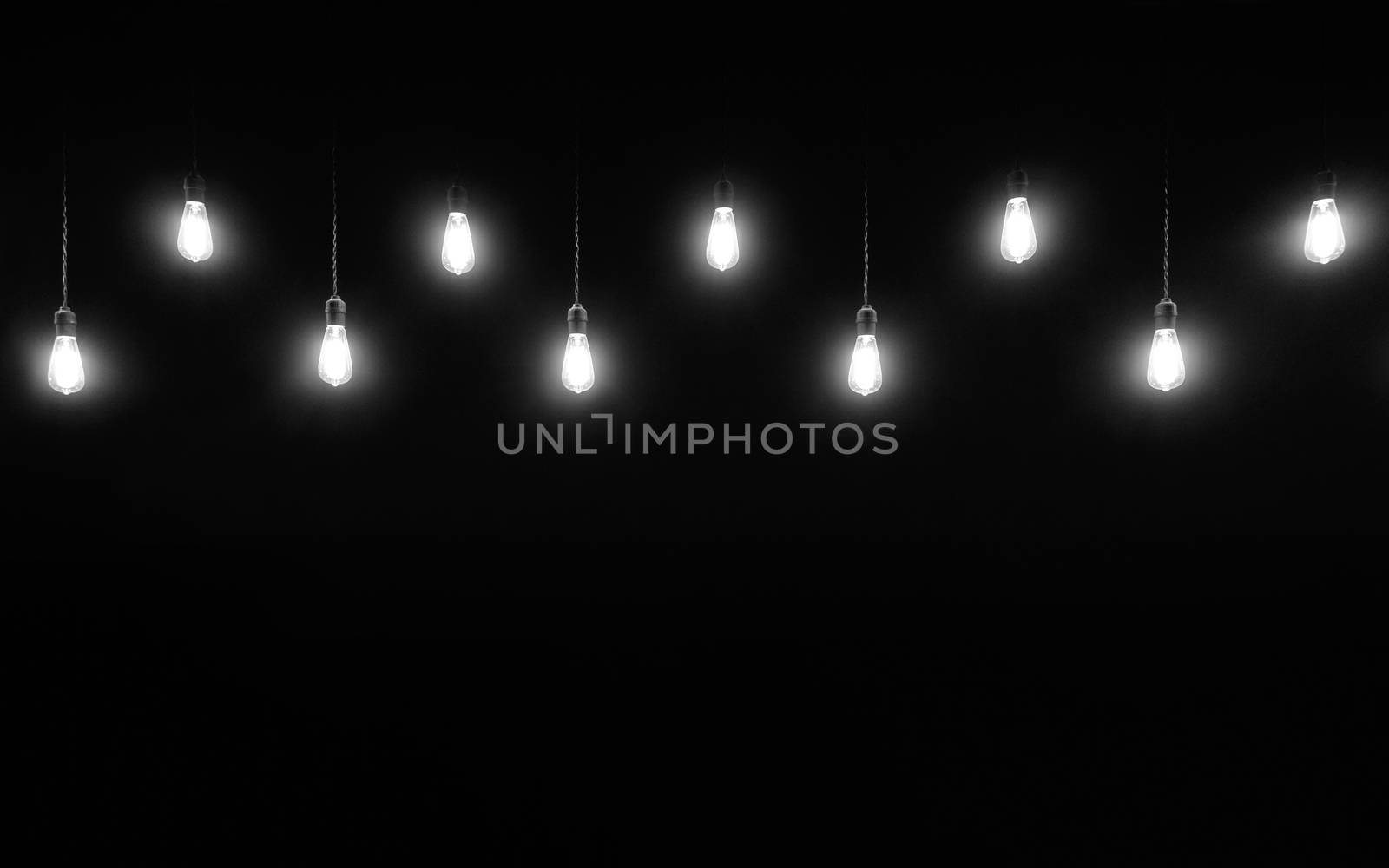 Hanging light bulbs on black background with copy space, black and white photography