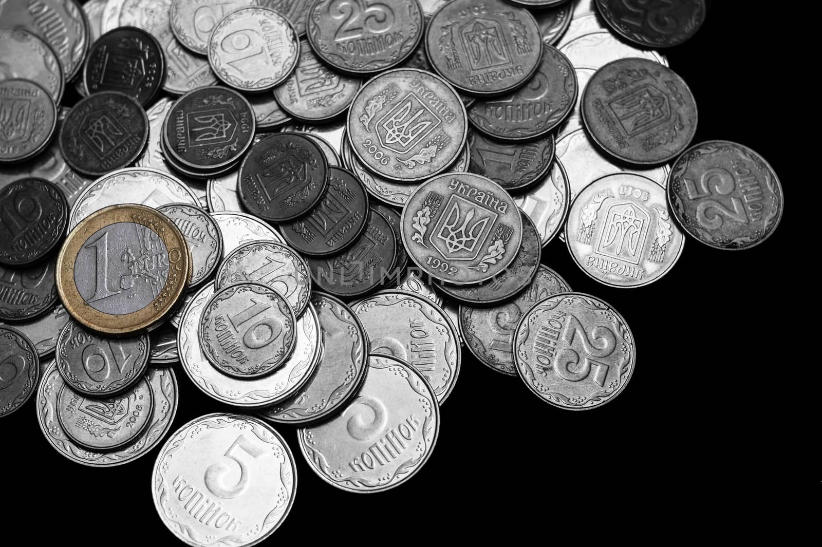 Ukrainian coins with one euro coin isolated on black background. Black and white image.  Euro coin is colored. Close-up view. Coins are located at the left side of frame. A conceptual image.