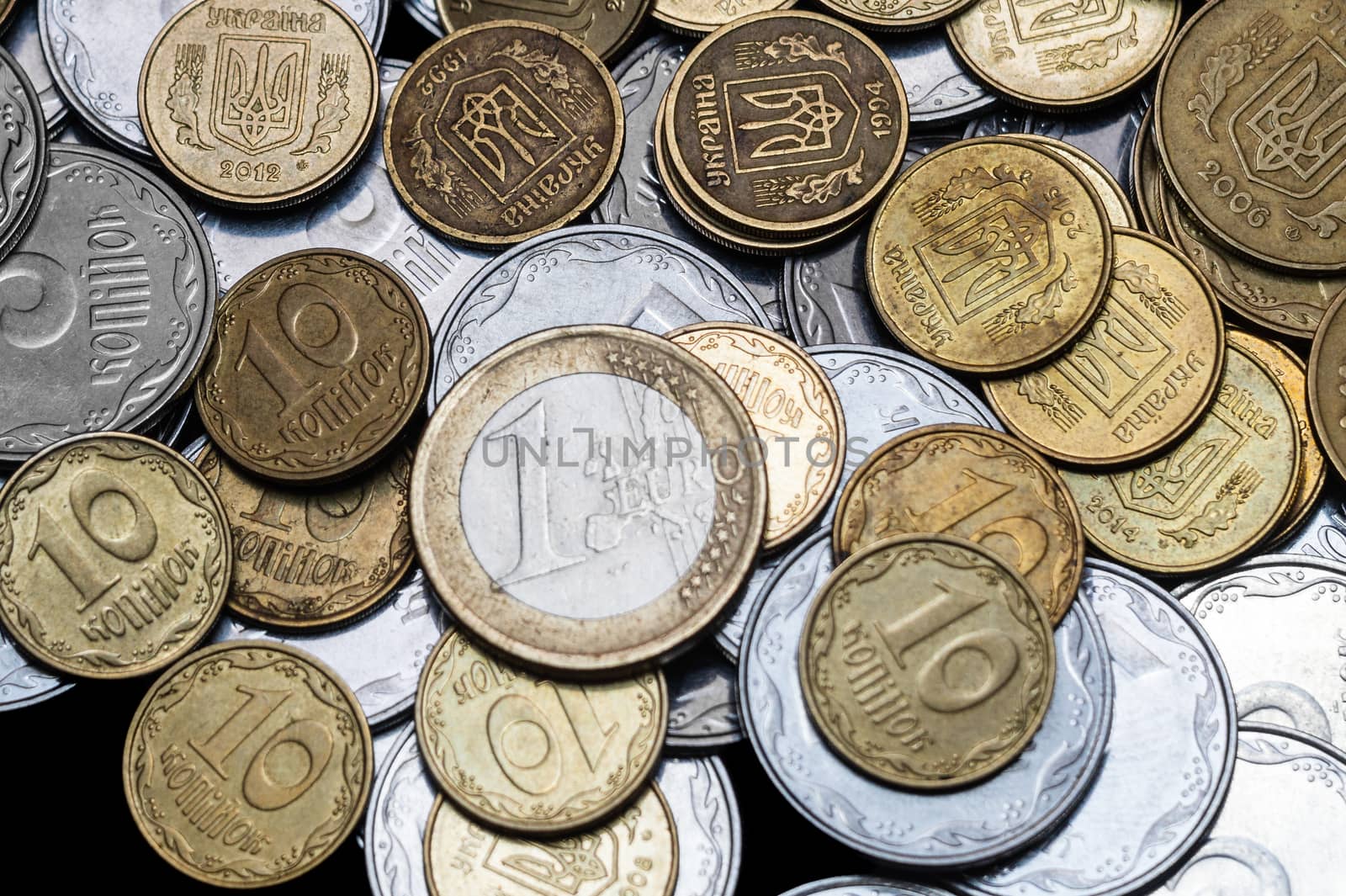 Ukrainian coins with one euro coin isolated on black background. Close-up view. Coins are located at center of frame. A conceptual image.