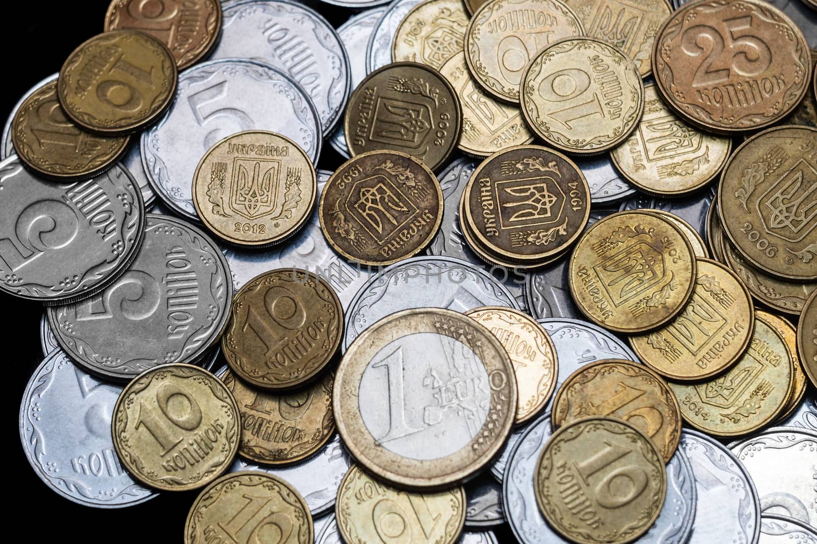 Ukrainian coins with one euro coin isolated on black background. Close-up view. Coins are located at center of frame. A conceptual image.