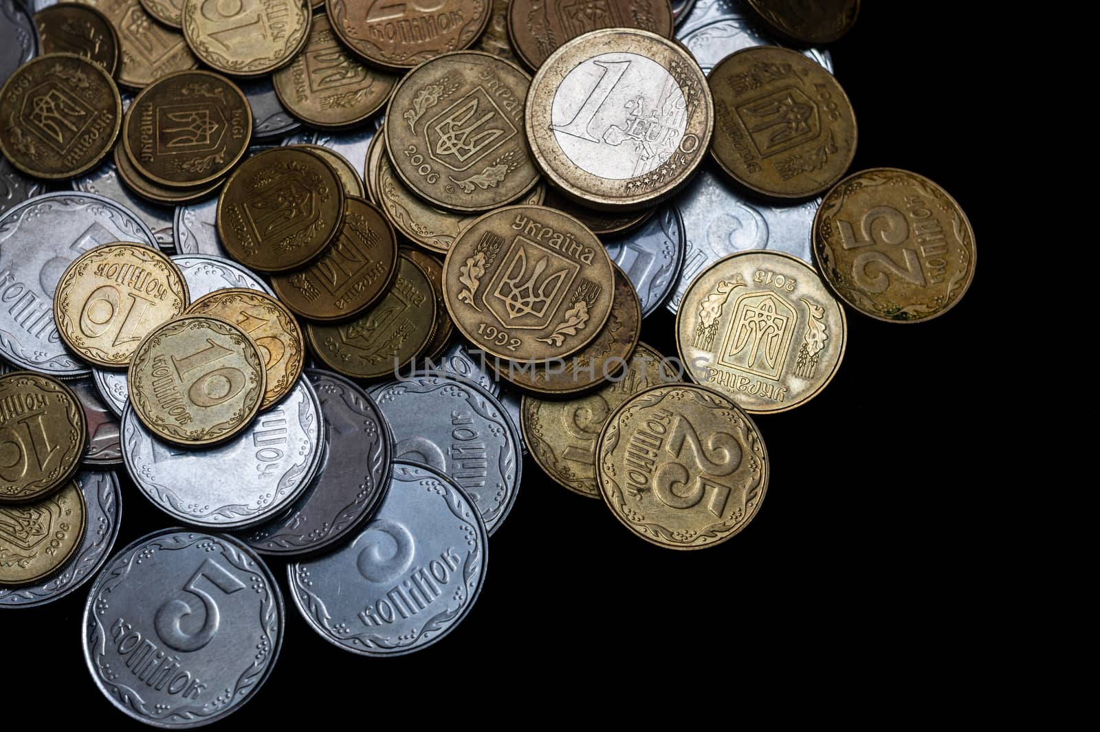 Ukrainian coins with one euro coin isolated on black background. Close-up view. Coins are located at the left side of frame. A conceptual image.