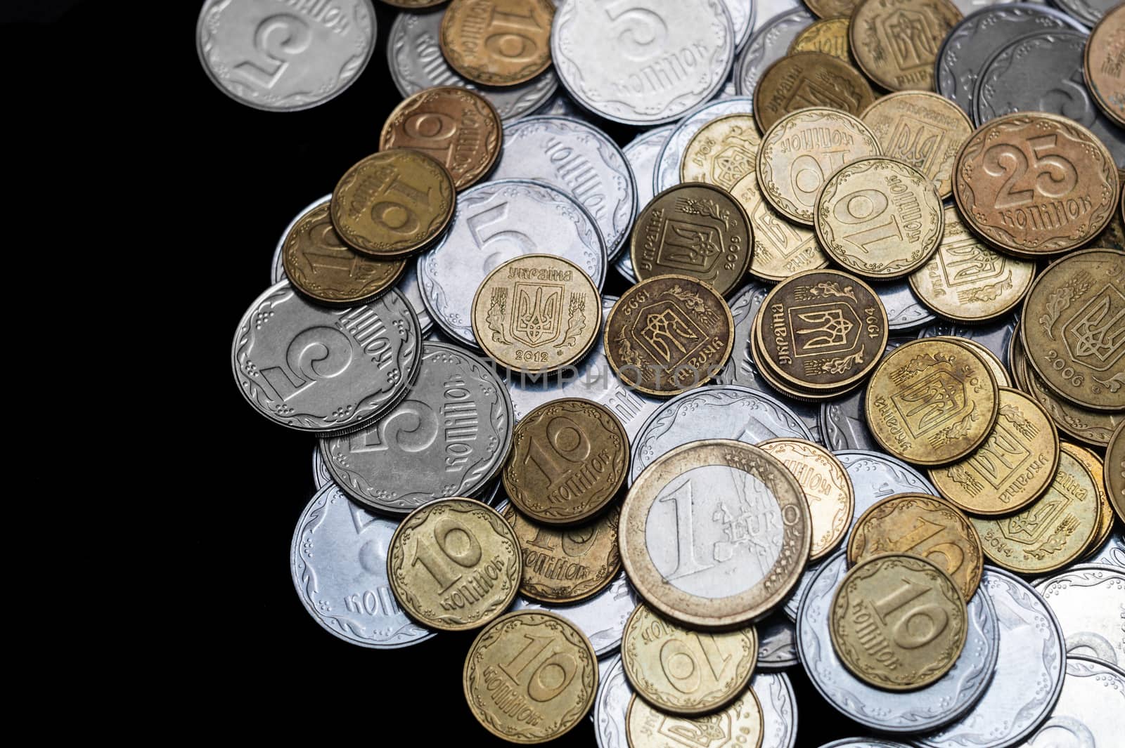 Ukrainian coins with one euro coin isolated on black background. Close-up view. Coins are located at the right side of frame. A conceptual image.