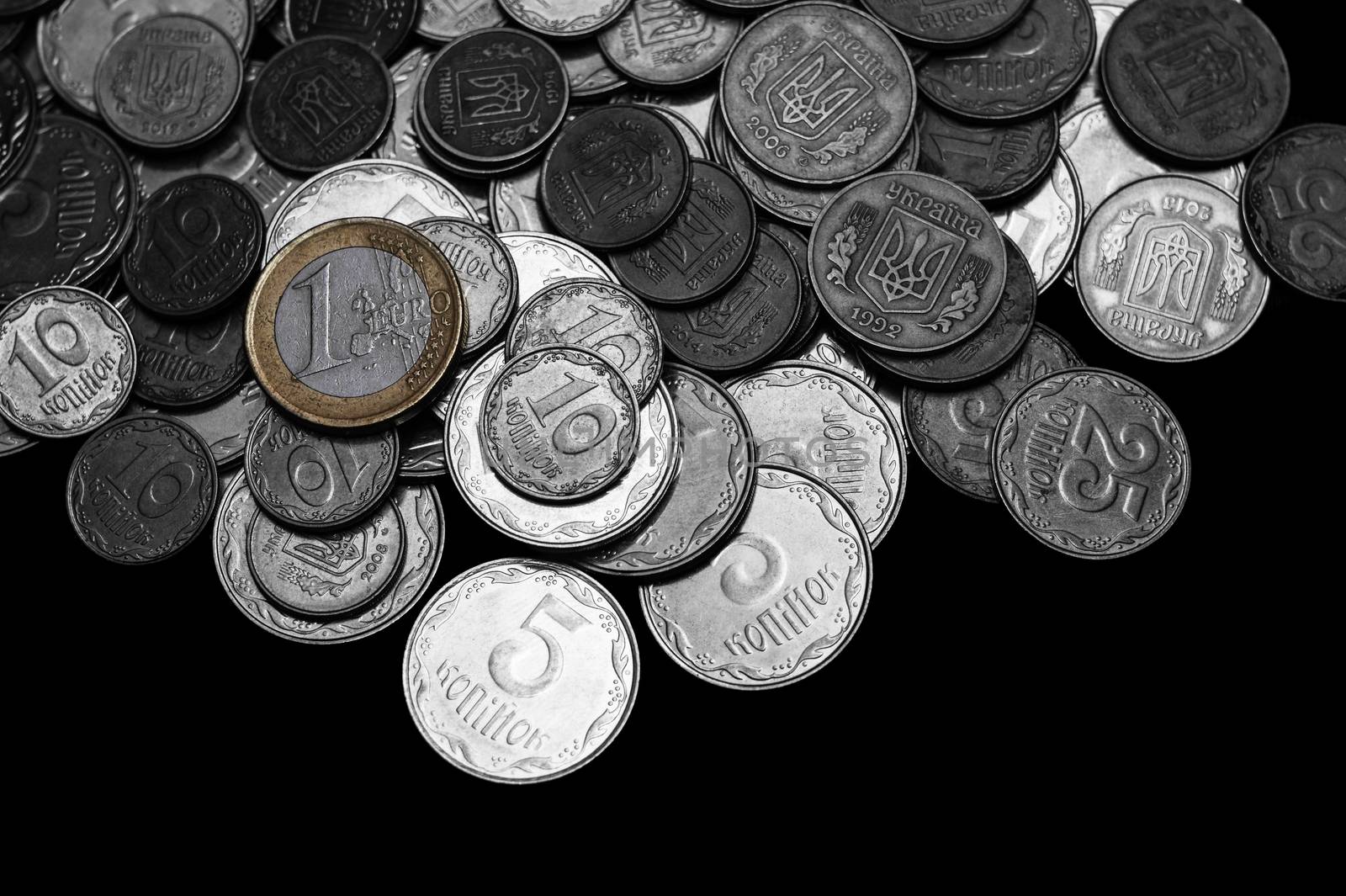 Ukrainian coins with one euro coin isolated on black background. Black and white image.  Euro coin is colored. Close-up view. Coins are located at the upper side of frame. A conceptual image. by alexsdriver