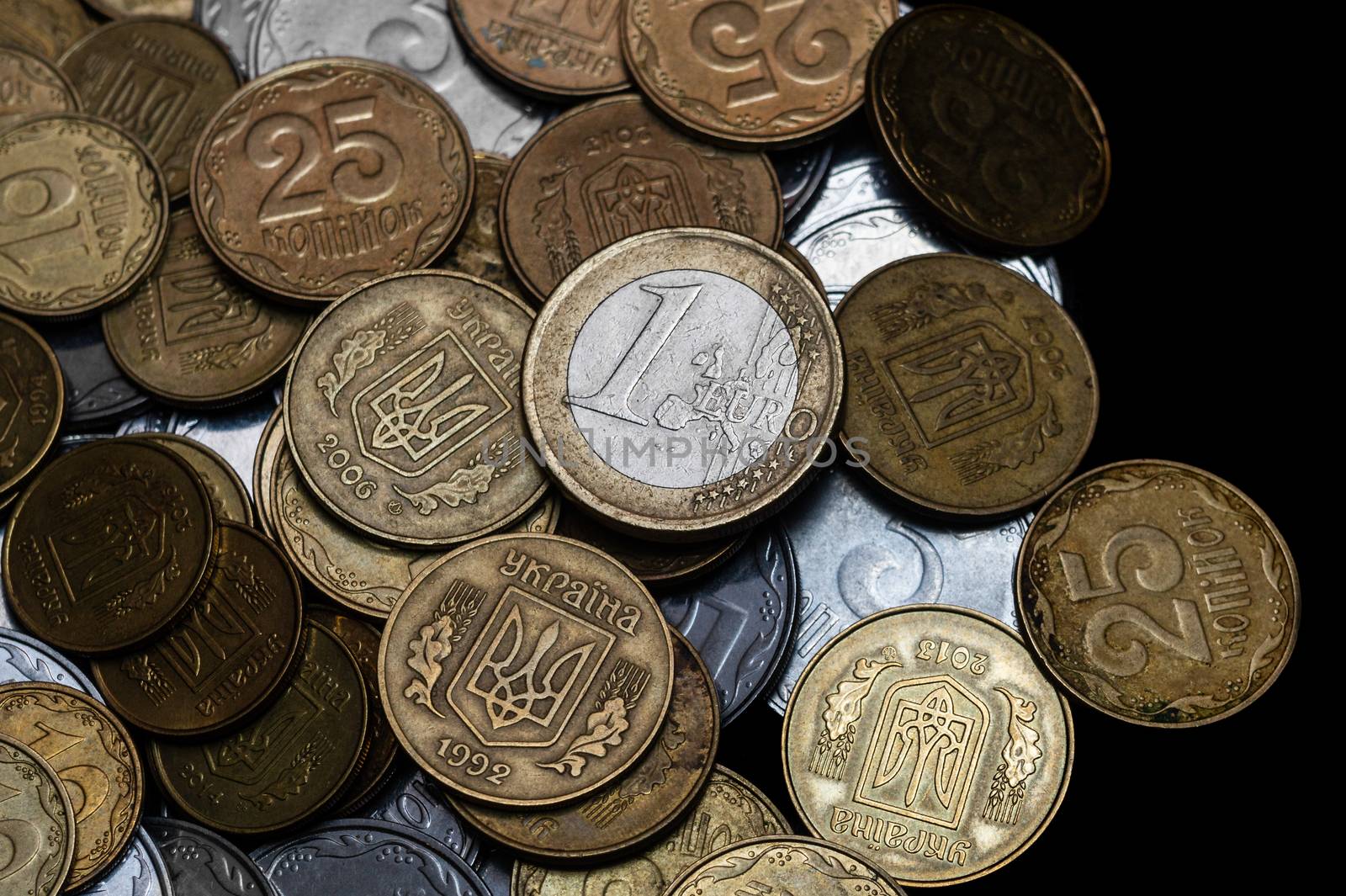 Ukrainian coins with one euro coin isolated on black background. Close-up view. Coins are located at center of frame. A conceptual image.