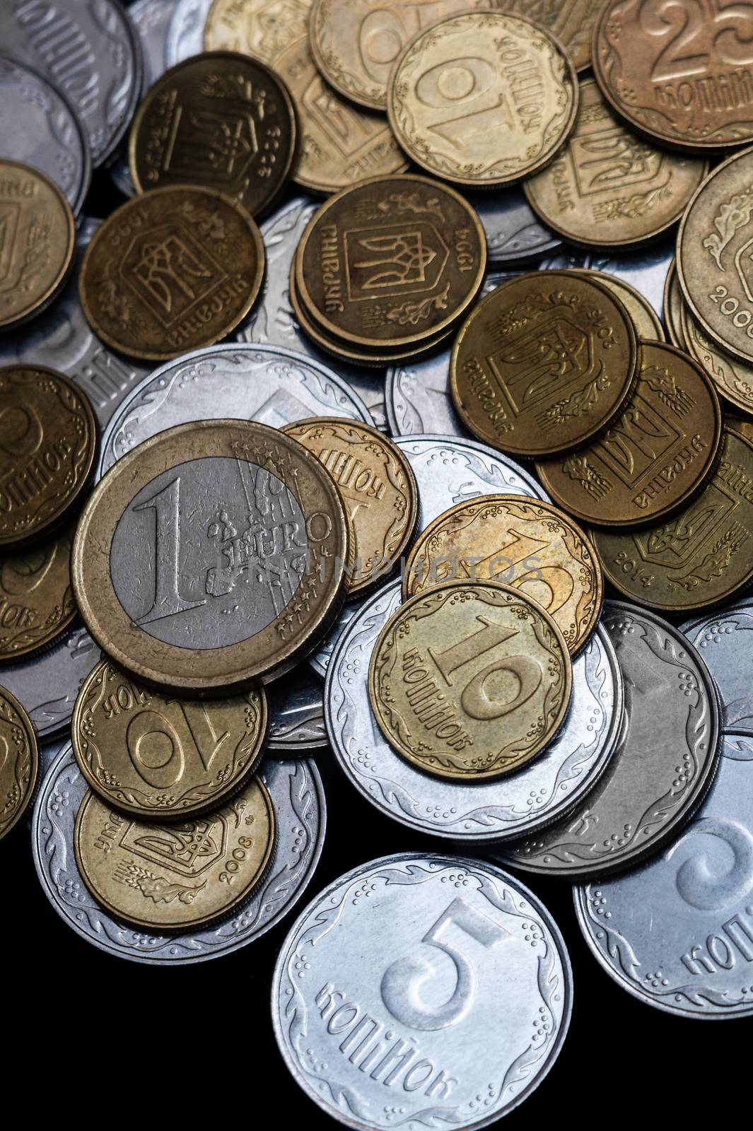 Ukrainian coins with one euro coin isolated on black background. Close-up view. Coins are located at the upper side of frame. A conceptual image.
