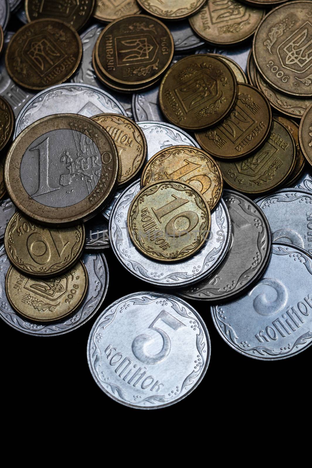Ukrainian coins with one euro coin isolated on black background. Close-up view. Coins are located at the upper side of frame. A conceptual image.