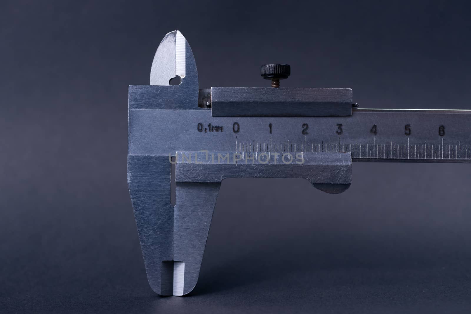 Vintage steel caliper tool closeup. Caliper tips and scale in focus. Tool in very good condition. Scale in metric units, milimeter step. Stock photo on blurred gray background.