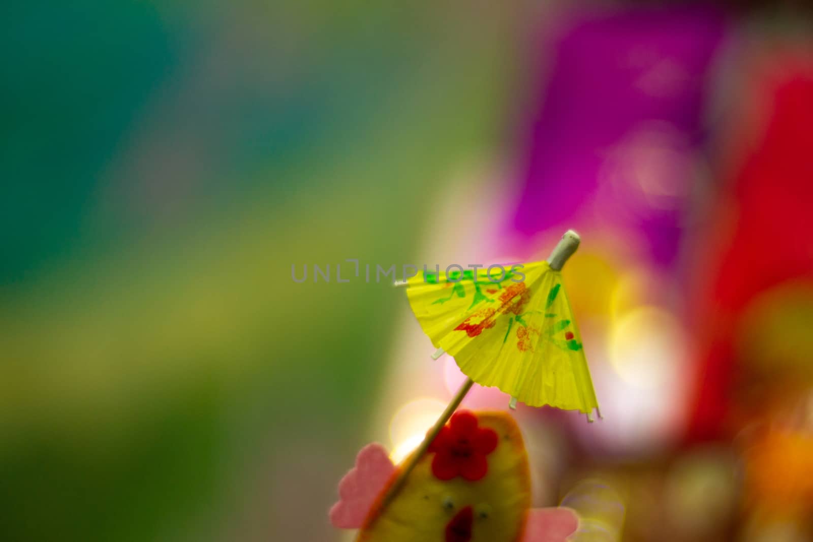 Yellow cocktail paper umbrella on colorful blurred defocused background.