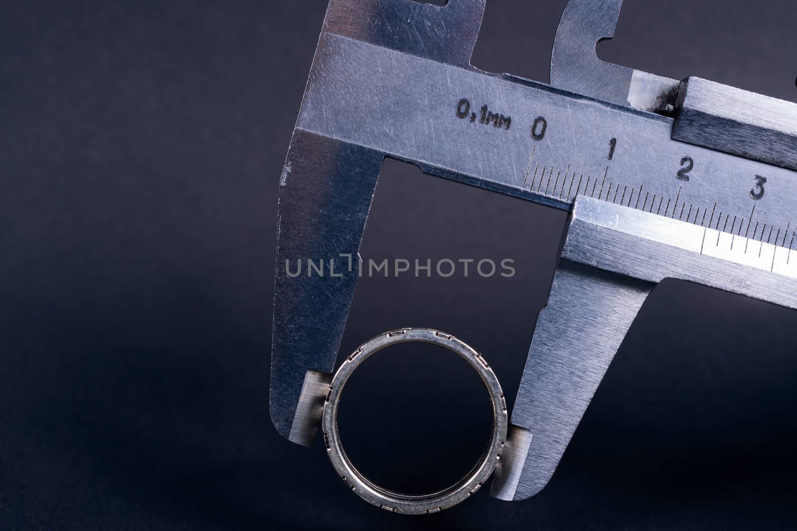 Vintage steel caliper measuring sterling silver male ring closeup. Scale and ring in focus. Tool in very good condition. Scale in metric units, milimeter step. Stock photo on blurred gray background.