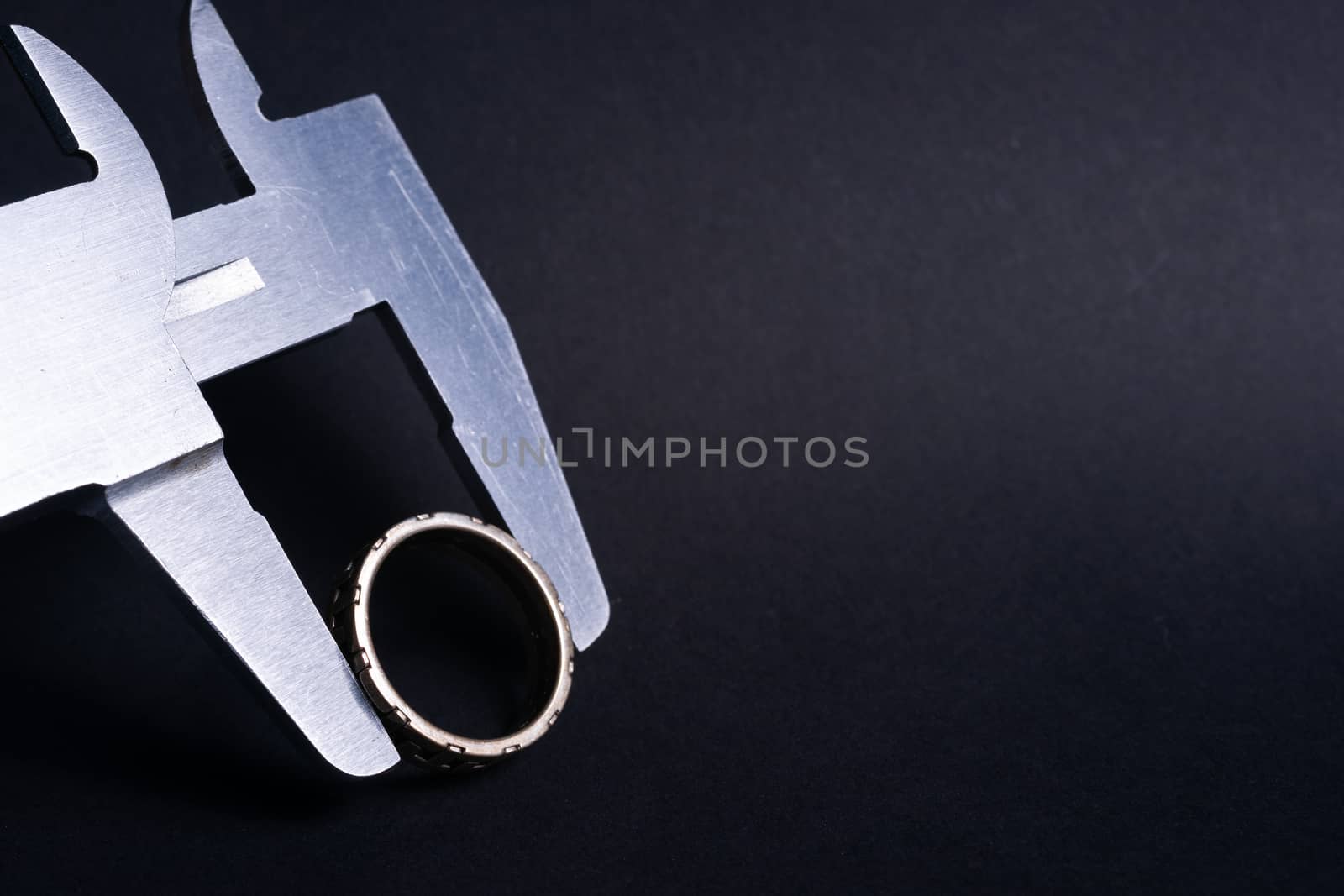 Vintage steel caliper measuring diameter of sterling silver male ring closeup. Ring in focus. Tool in very good condition. Stock photo on blurred dark gray background.