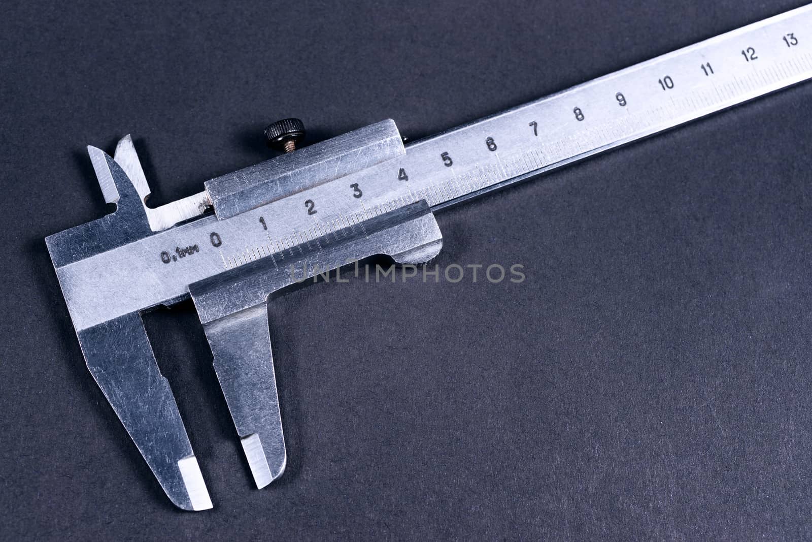 Vintage steel caliper on dark background. Scale in focus. Tool in very good condition. Stock photo on blurred gray background.