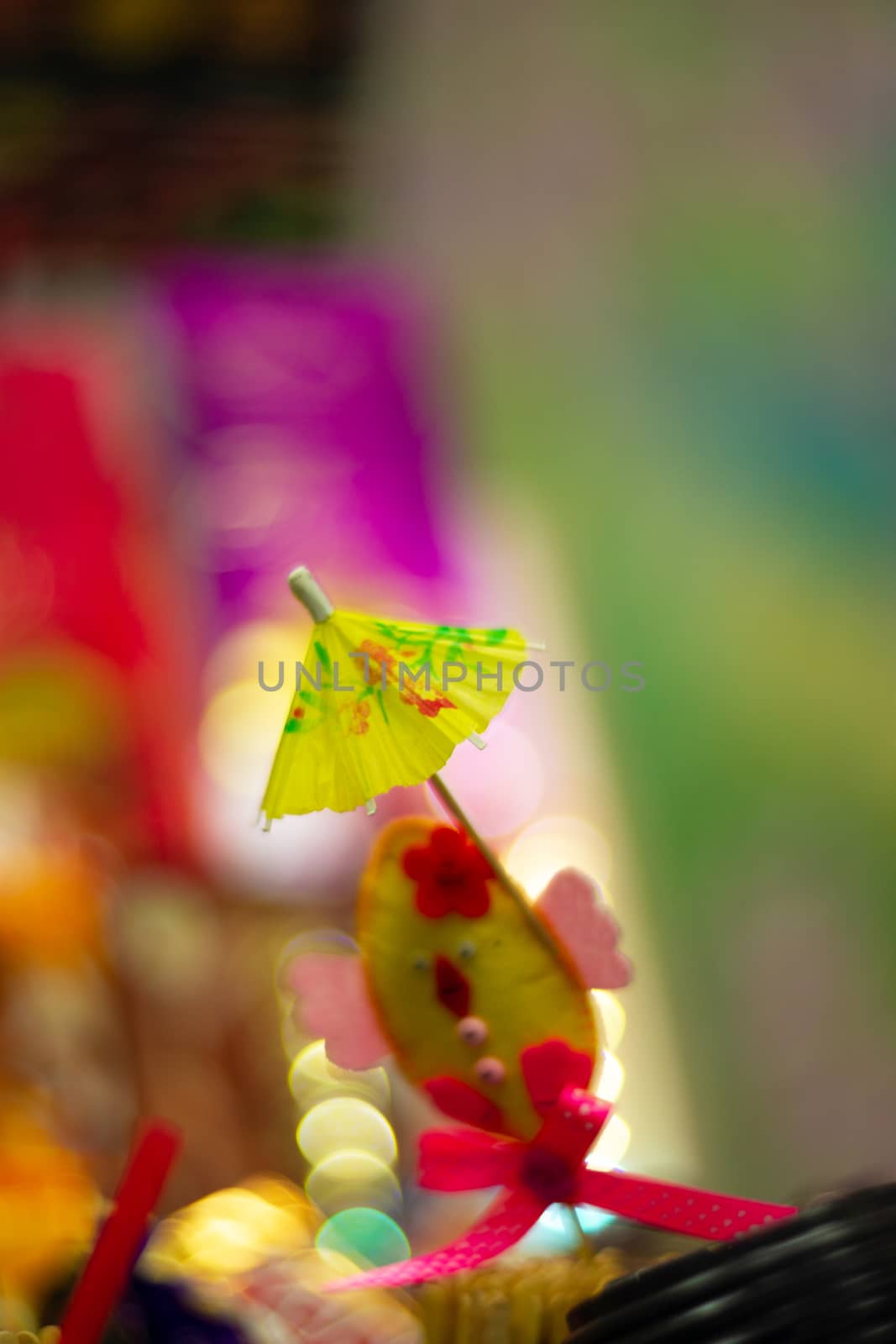 Yellow cocktail paper umbrella on colorful blurred defocused background.