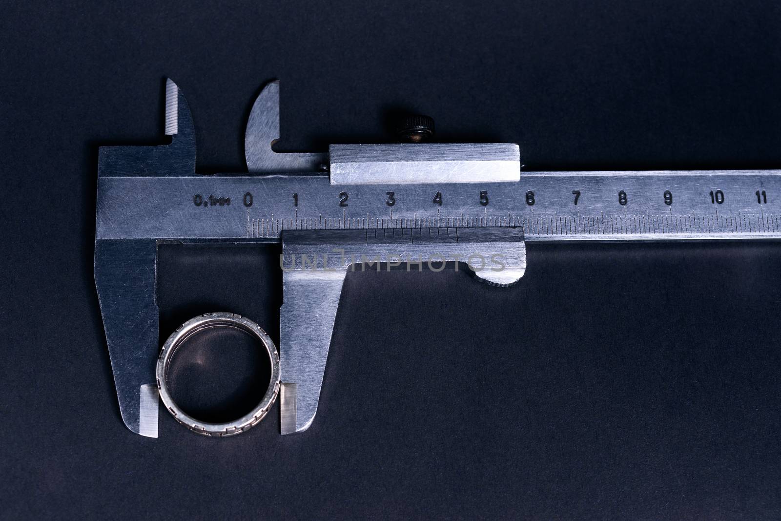 Vintage steel caliper measuring sterling silver male ring closeup. Scale and ring in focus. Tool in very good condition. Scale in metric units, milimeter step. Stock photo on blurred gray background.