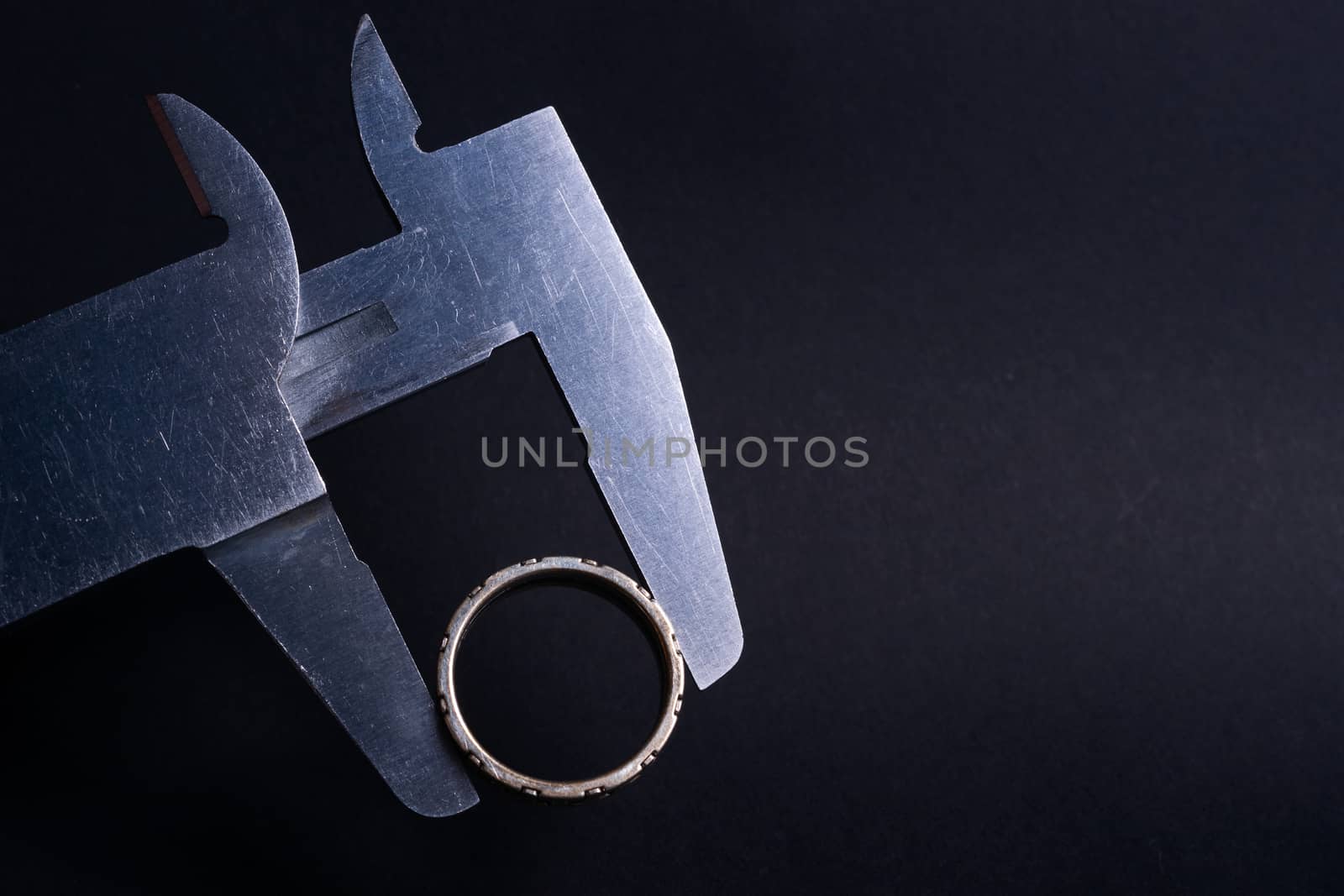 Vintage steel caliper measuring diameter of sterling silver male ring closeup. Ring in focus. Tool in very good condition. Stock photo on blurred dark gray background.