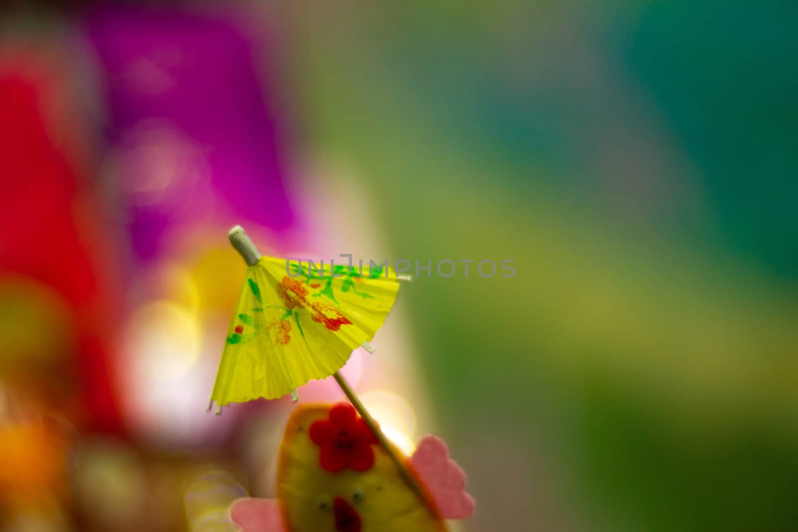 Yellow cocktail paper umbrella on colorful blurred defocused background.