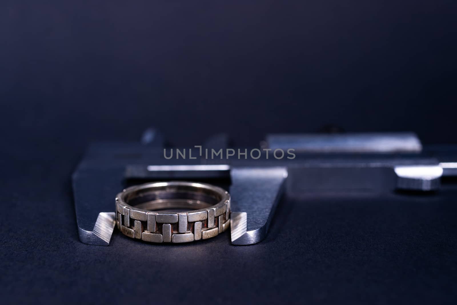 Vintage steel caliper measuring sterling silver male ring closeup. Ring in focus. Tool in very good condition. Stock photo on blurred gray background.