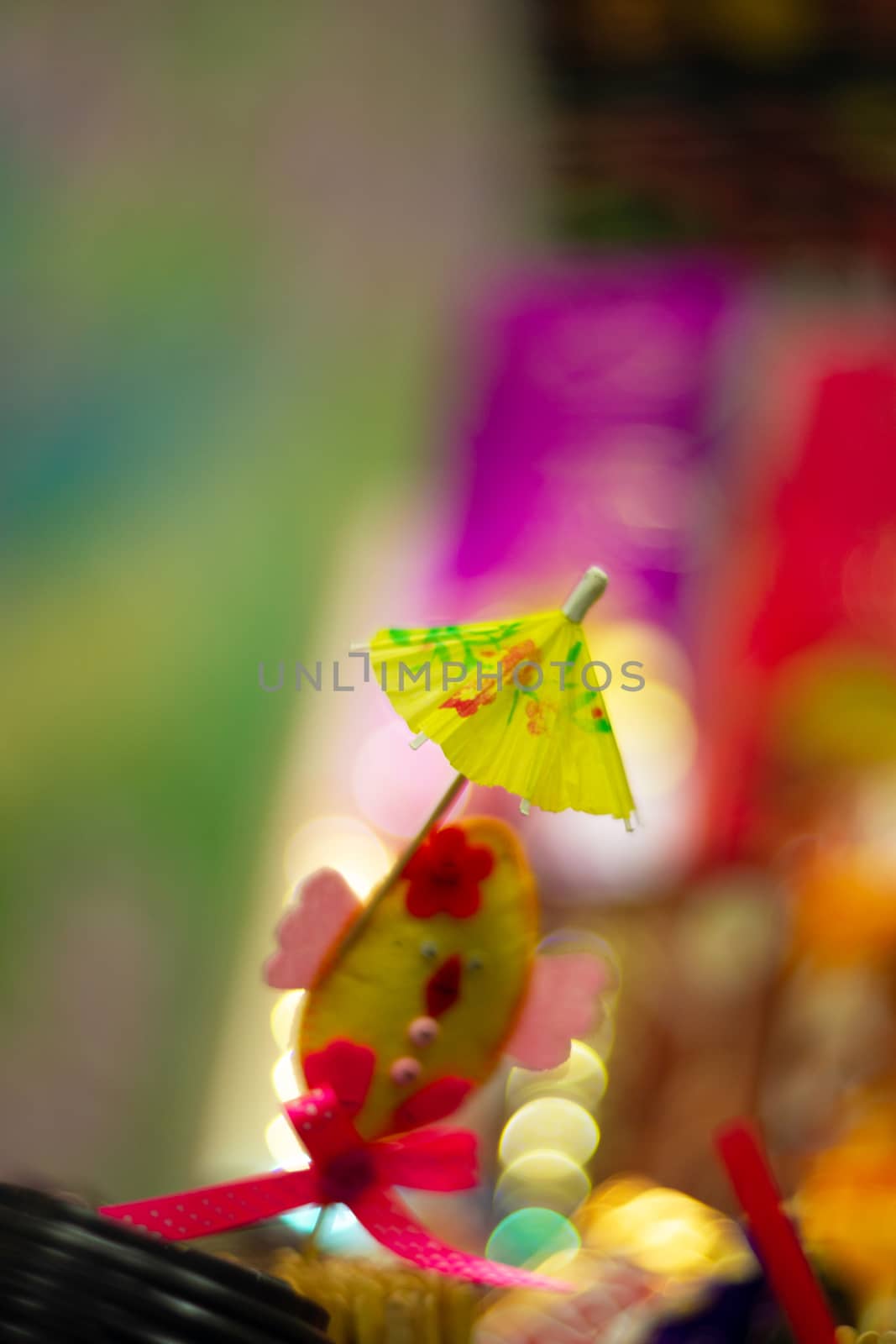 Yellow cocktail paper umbrella on colorful blurred defocused background.