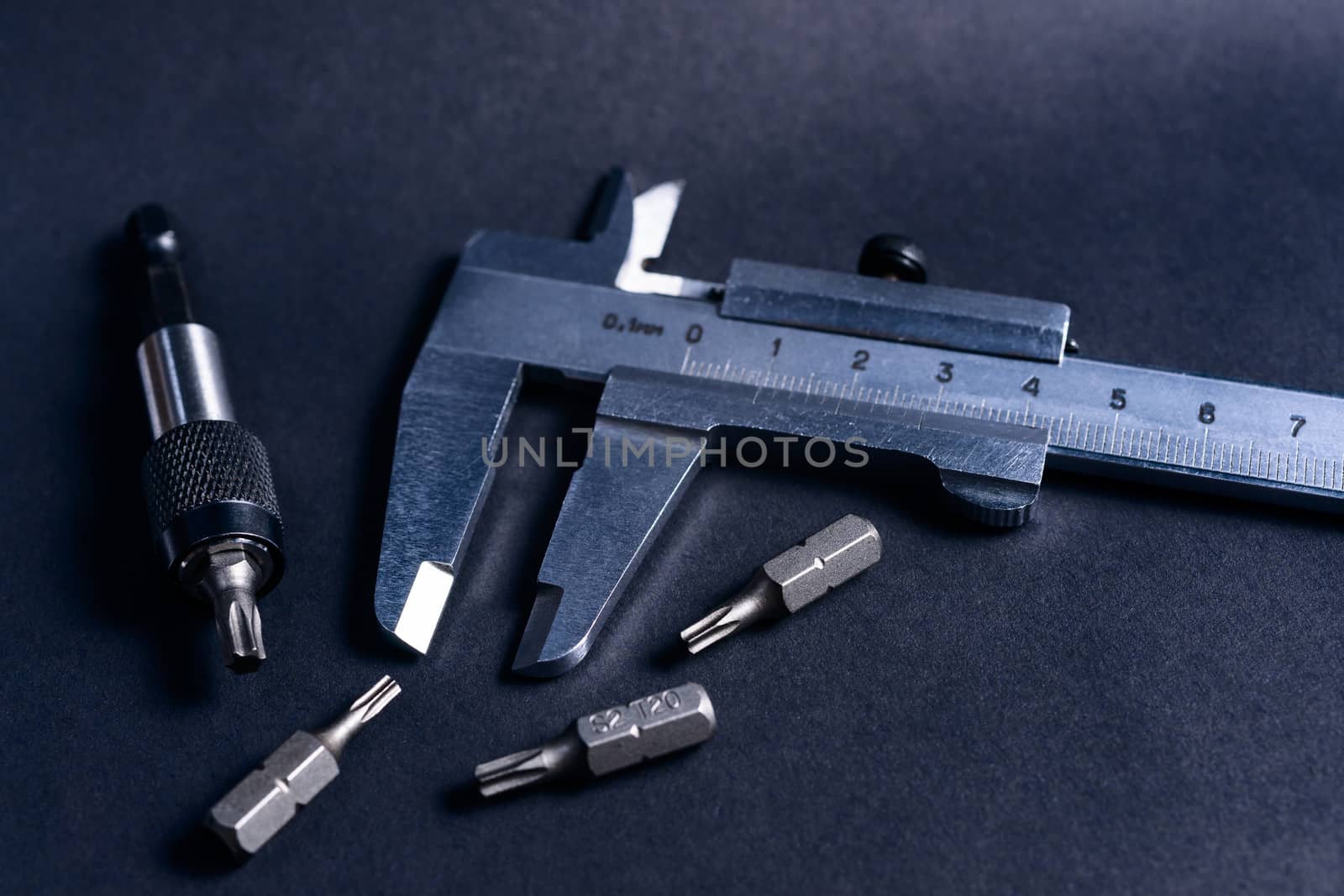 Vintage steel caliper with modern tool bits and bitholder on dark background. Caliper and bitholder in focus. Tools in very good condition. Stock photo on blurred dark gray background.
