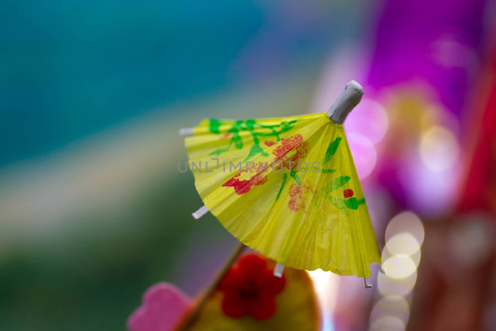Yellow cocktail paper umbrella on colorful blurred defocused background.