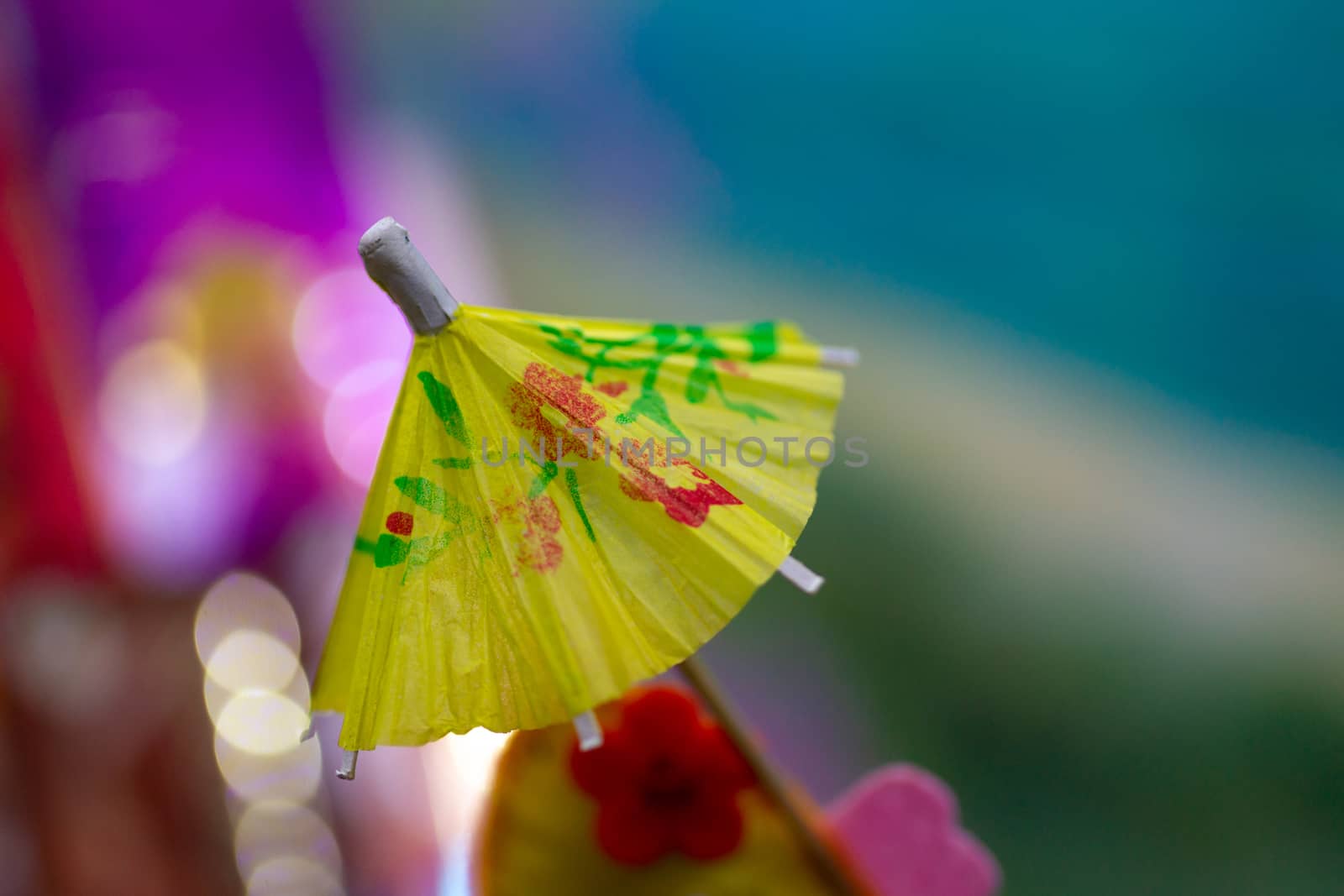 Yellow cocktail paper umbrella on colorful blurred defocused background.