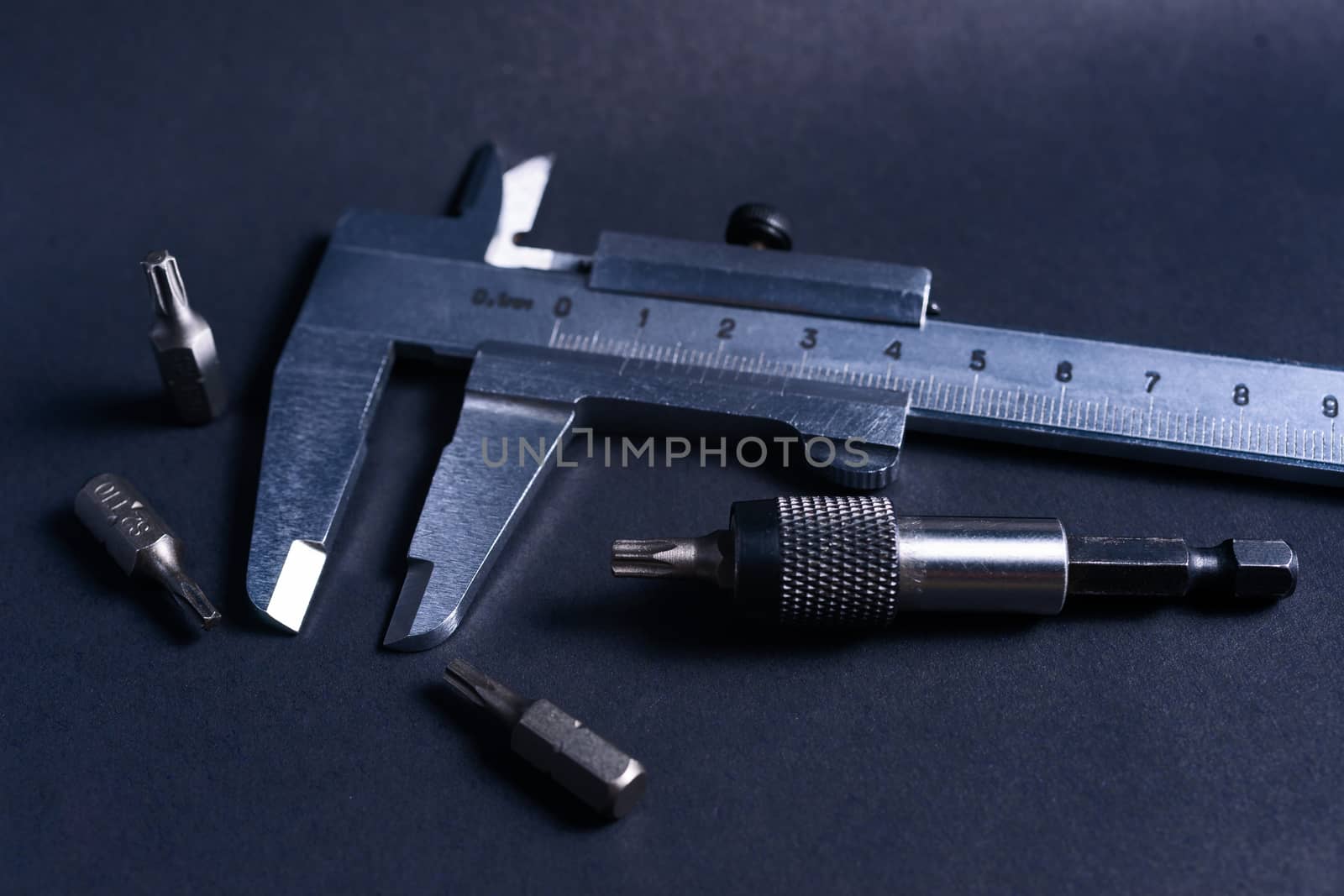 Vintage steel caliper with modern tool bits and bitholder on dark background. Caliper and bitholder in focus. Tools in very good condition. Stock photo on blurred dark gray background.