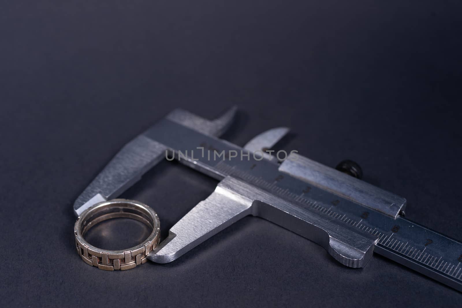 Vintage steel caliper measuring sterling silver male ring closeup. Ring in focus. Tool in very good condition. Stock photo on blurred gray background.