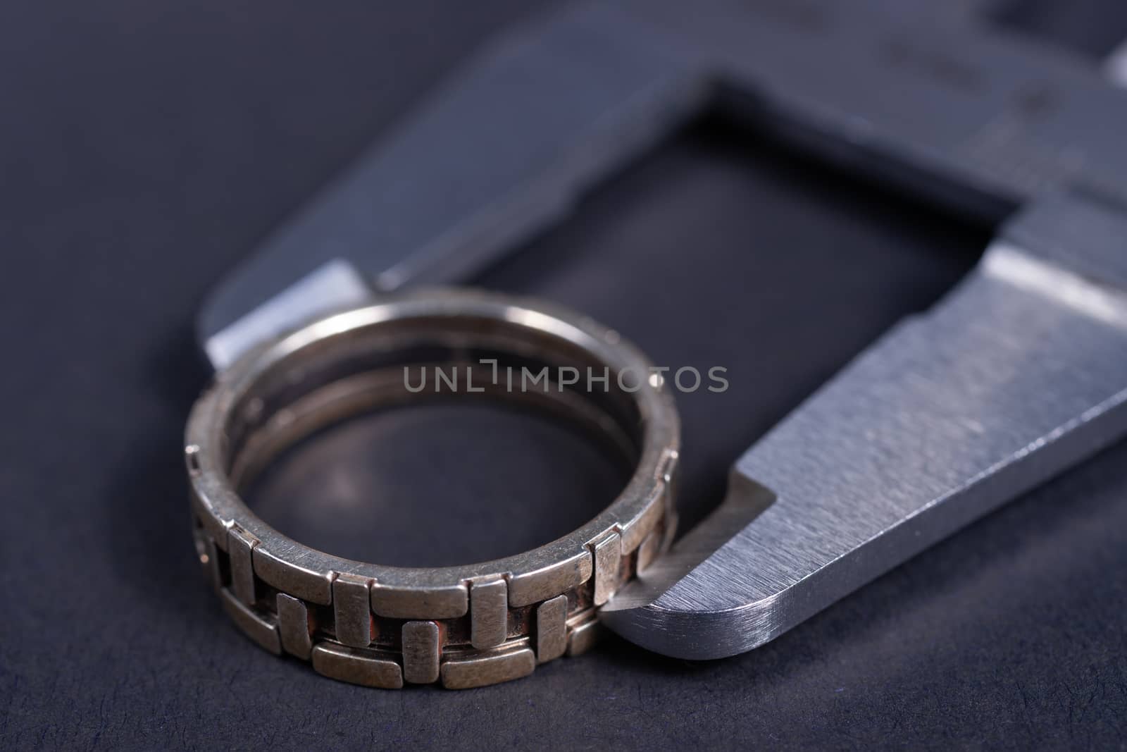Vintage steel caliper measuring sterling silver male ring closeup. Ring in focus. Tool in very good condition. Stock photo on blurred gray background.