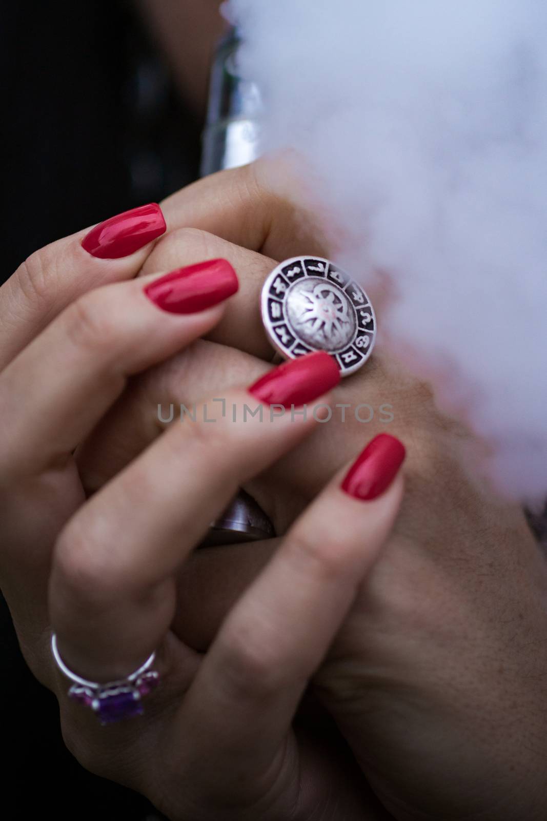 Caucasian woman with red nails manicure and antique ring on finger holds small vape. Smoking alternative vay. Woman exhales thick smoke. Life without cigarettes. Woman-vaper. Small e-cigarette.