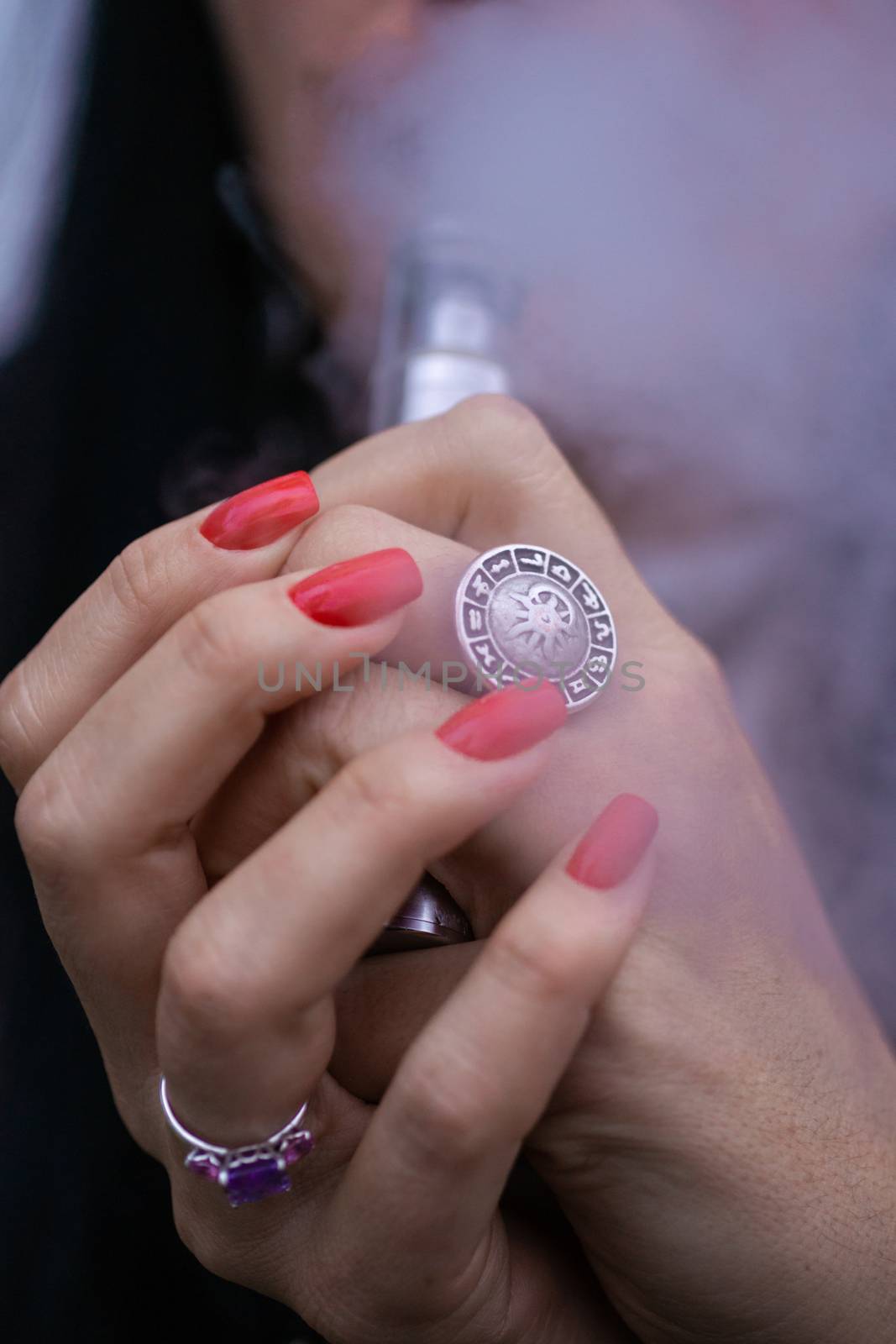 Caucasian woman with red nails manicure and antique ring on finger holds small vape. Smoking alternative vay. Woman exhales thick smoke. Life without cigarettes. Woman-vaper. Small e-cigarette. by alexsdriver