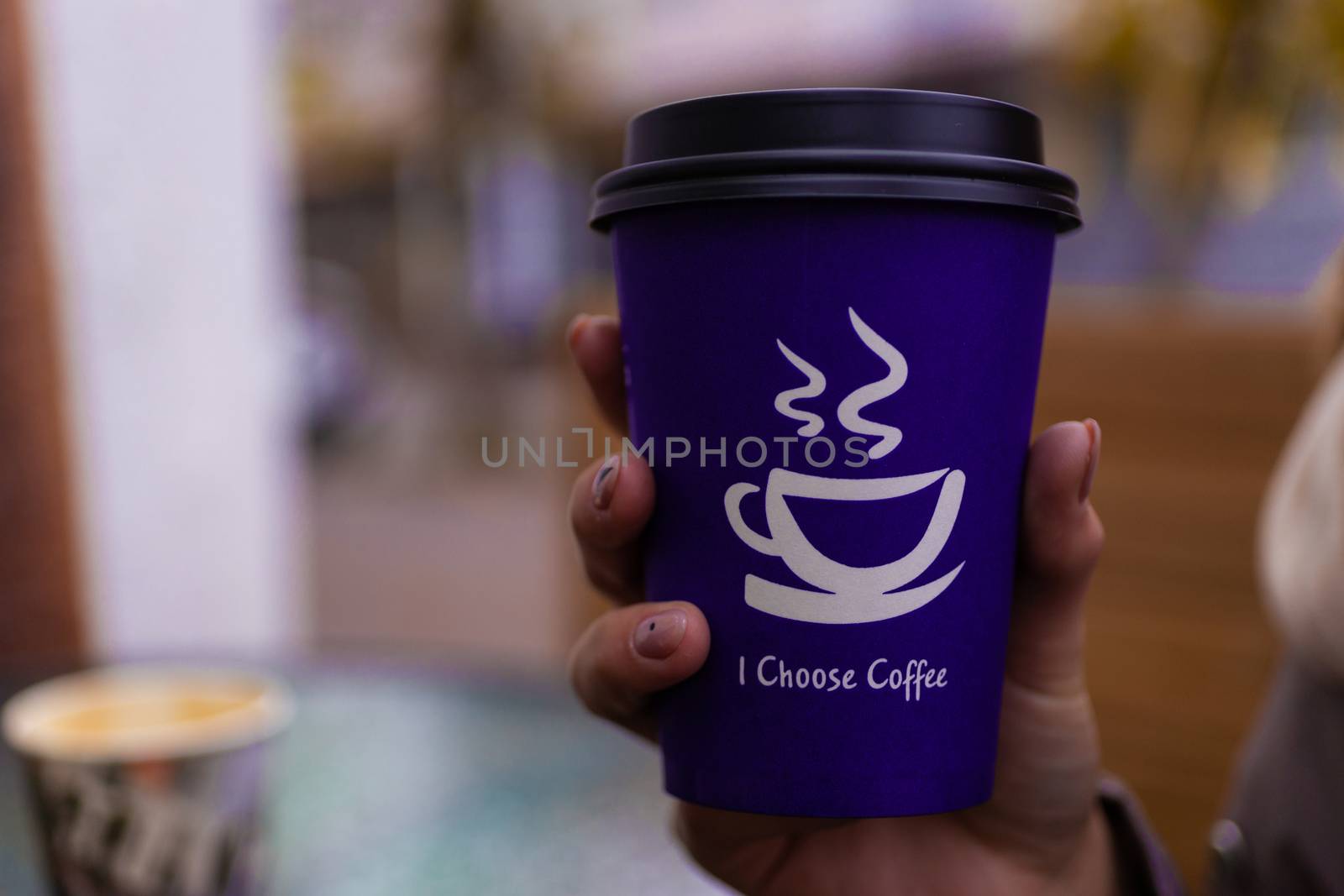 Young 21y.o. woman holds purple coffee paper cup in hand. On cup wrote: "I choose coffee". Beginning a good day!