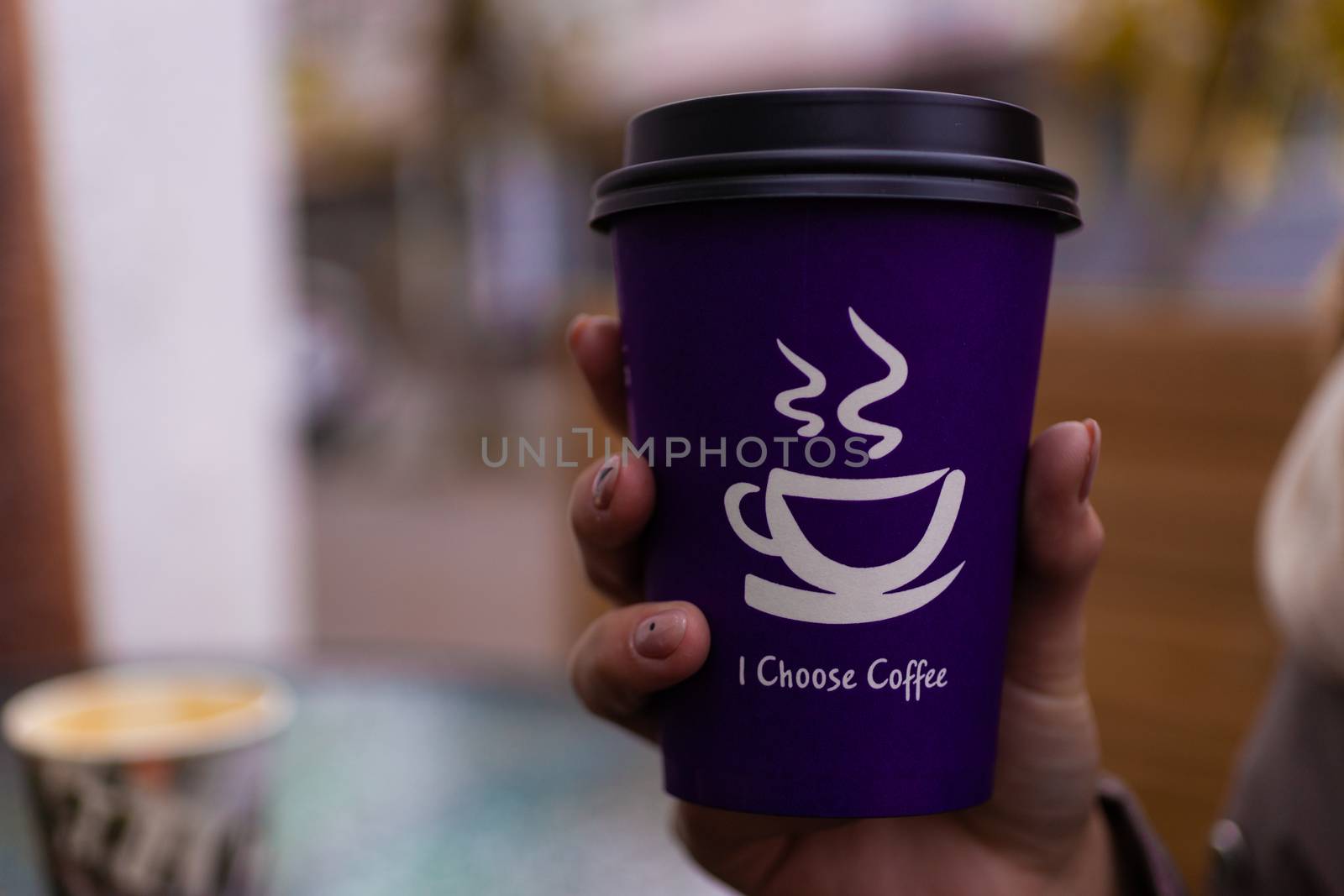 Young 21y.o. woman holds purple coffee paper cup in hand. On cup wrote: "I choose coffee". Beginning a good day!