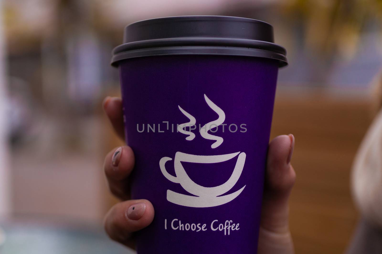 Young 21y.o. woman holds purple coffee paper cup in hand. On cup wrote: "I choose coffee". Beginning a good day!