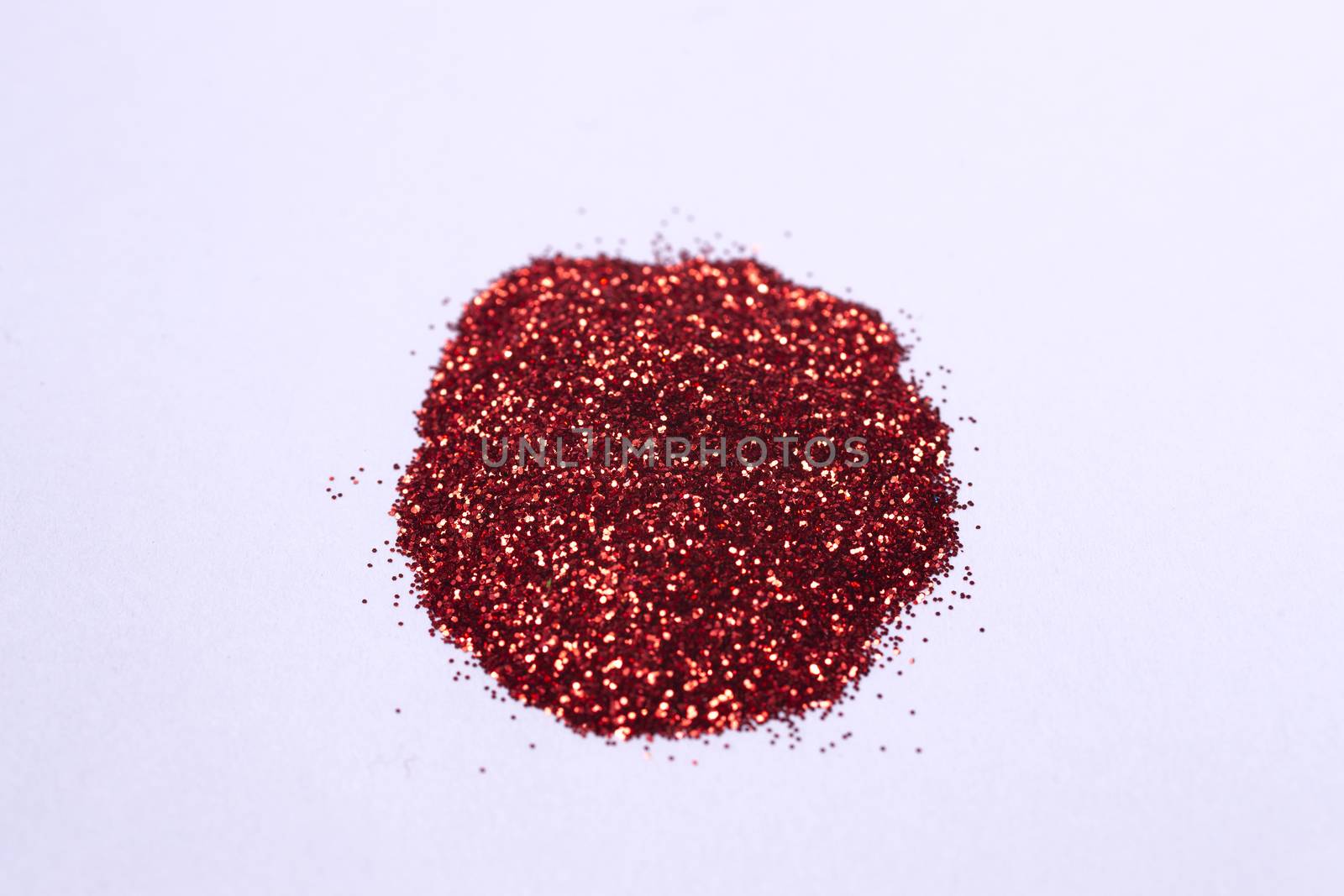 A small bunch of hue red nail gritter for manicure. Red glitter shining on daylight. Stock photo isolated on white background. Varnish topping.