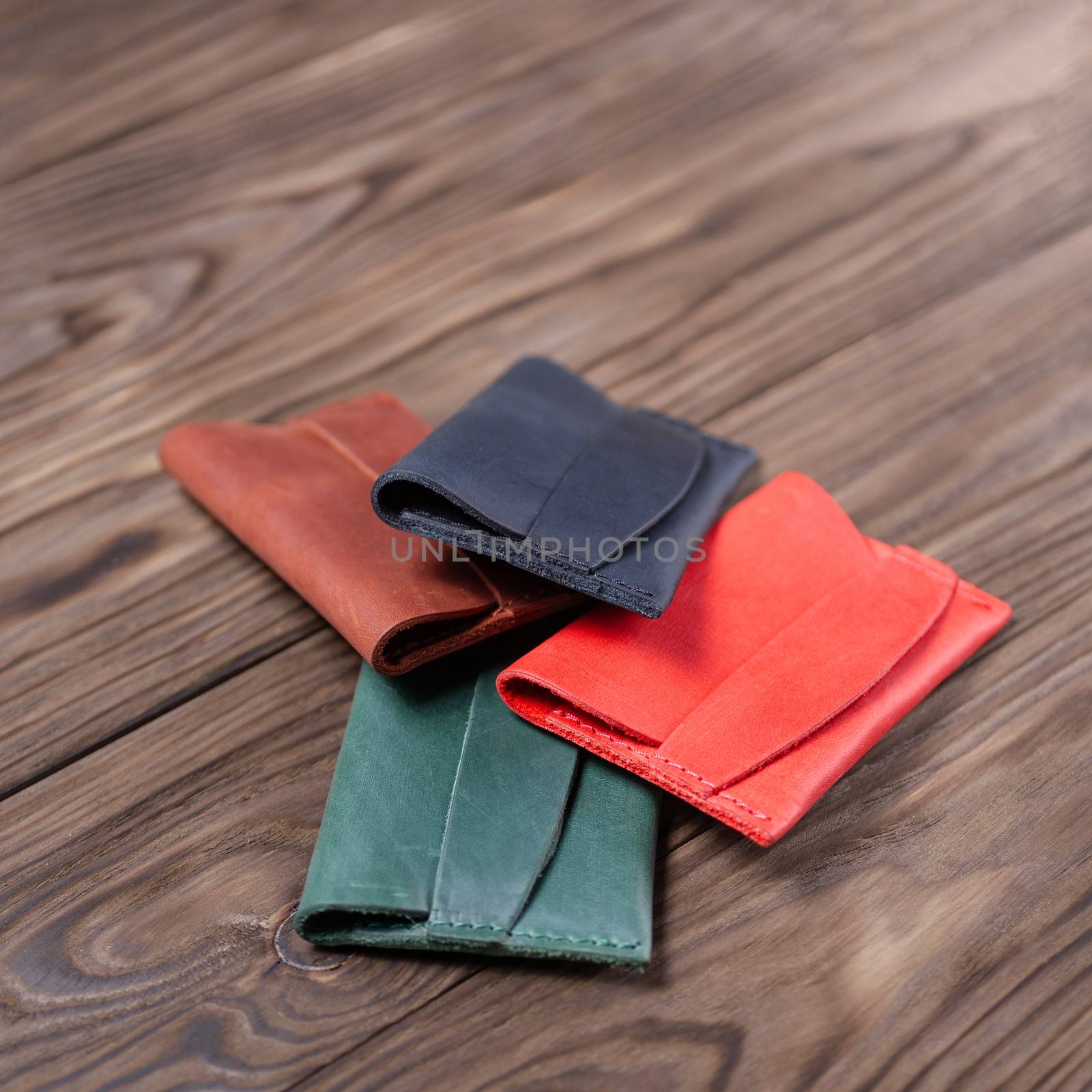 Flat lay photo of four different colour handmade leather one pocket cardholders.  Red, black, ginger and green colors. Stock photo on wooden background. 