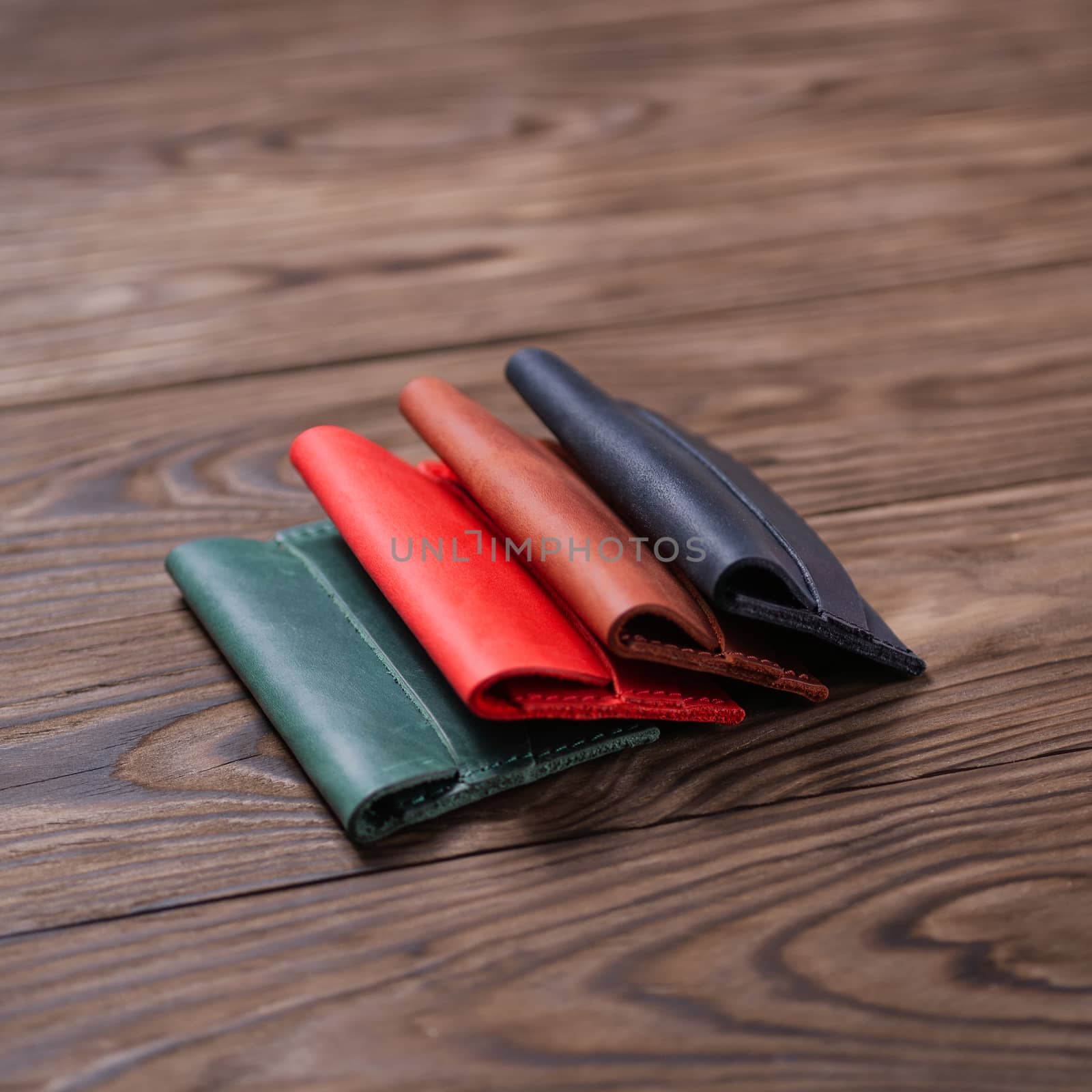 Flat lay photo of four different colour handmade leather one pocket cardholders.  Red, black, ginger and green colors. Stock photo on wooden background.