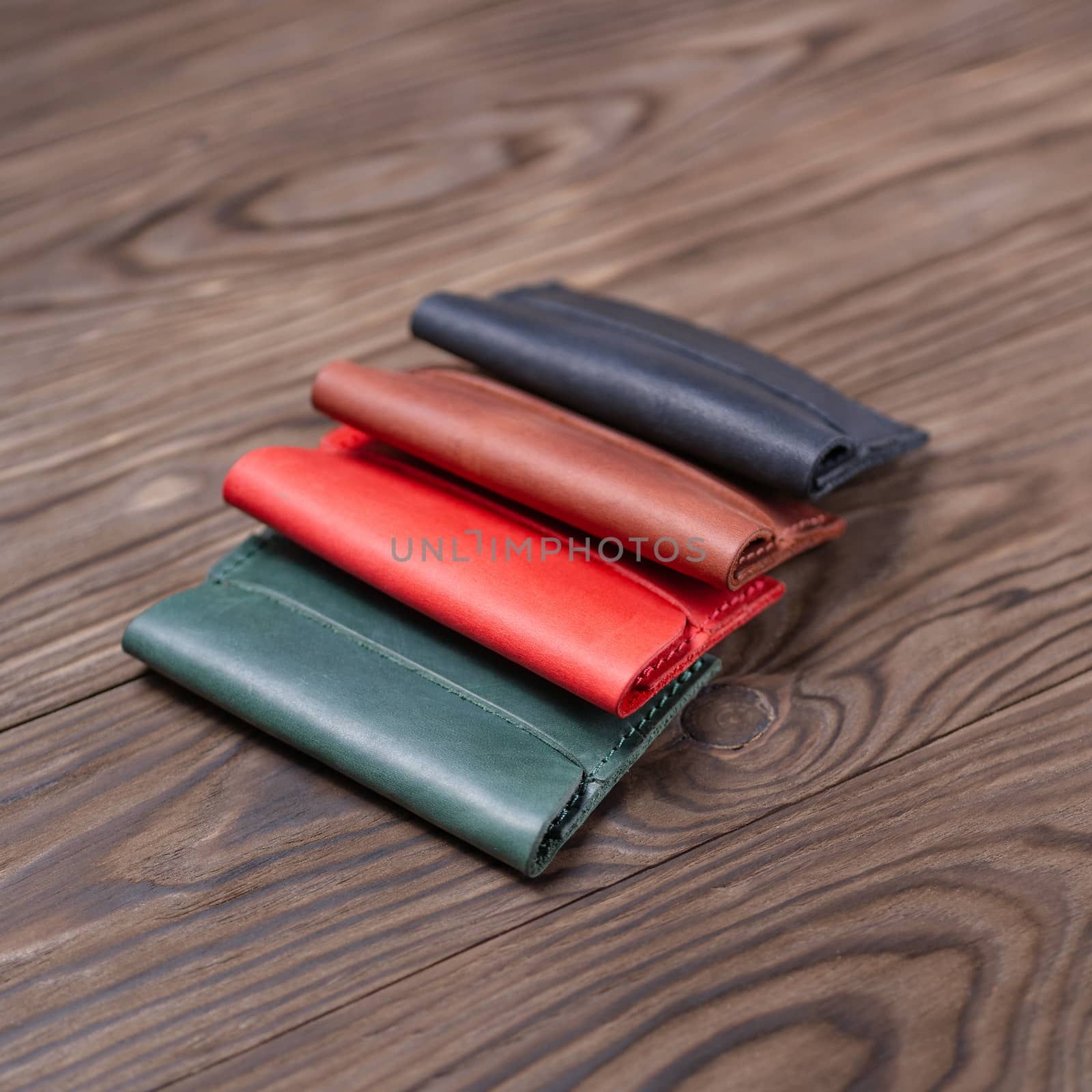 Flat lay photo of four different colour handmade leather one pocket cardholders.  Red, black, ginger and green colors. Stock photo on wooden background. by alexsdriver