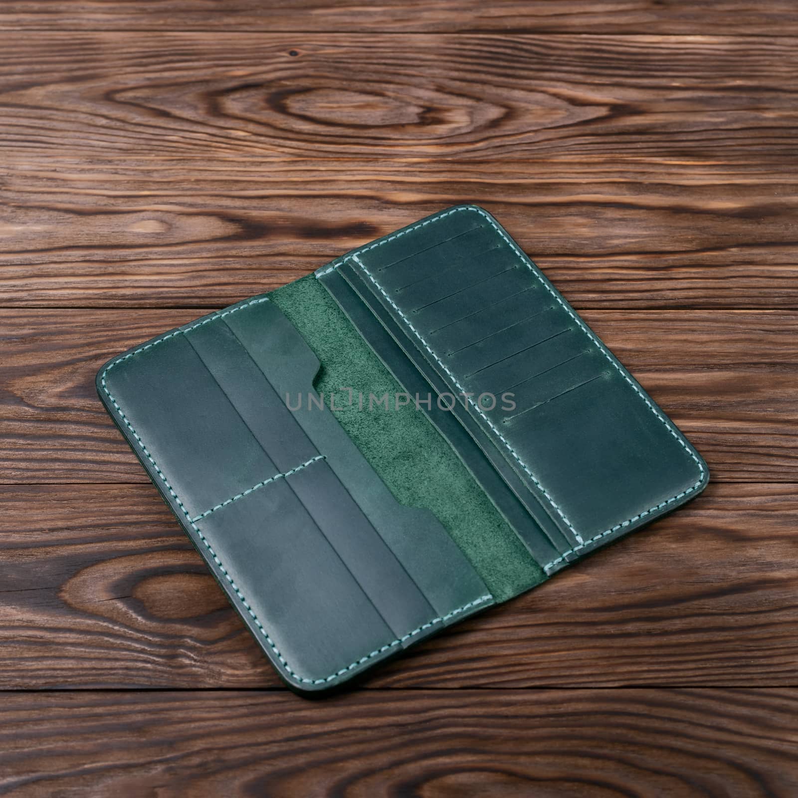 Green color handmade leather porte-monnaie on wooden textured background. Purse is opened and empty. Side view. Stock photo of luxury accessories. by alexsdriver